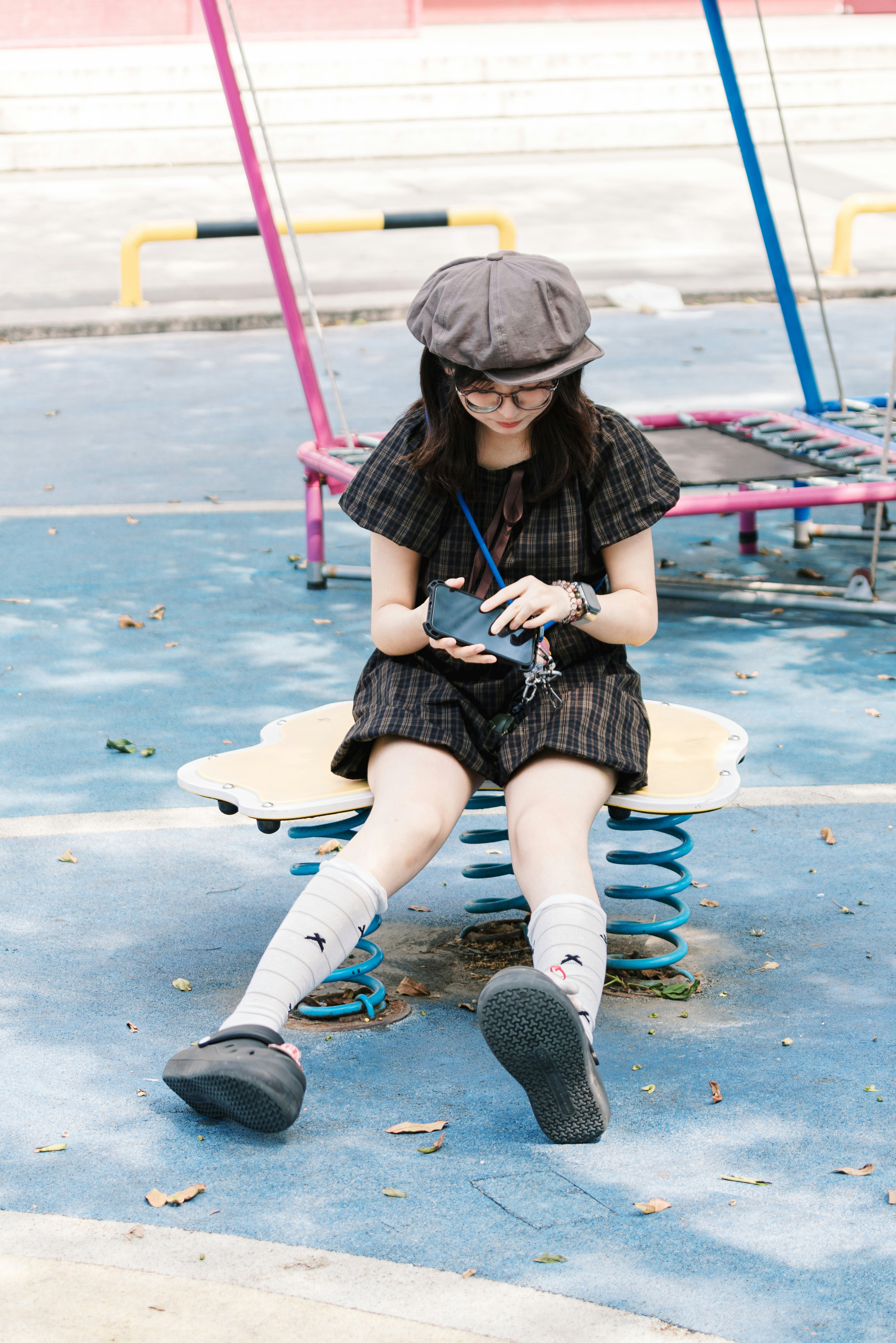 Young woman in cap and glasses on playground spring rider.