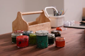 Colorful paint jars and art supplies on a wooden table.