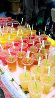 Many colorful iced drinks with straws on a market stall.