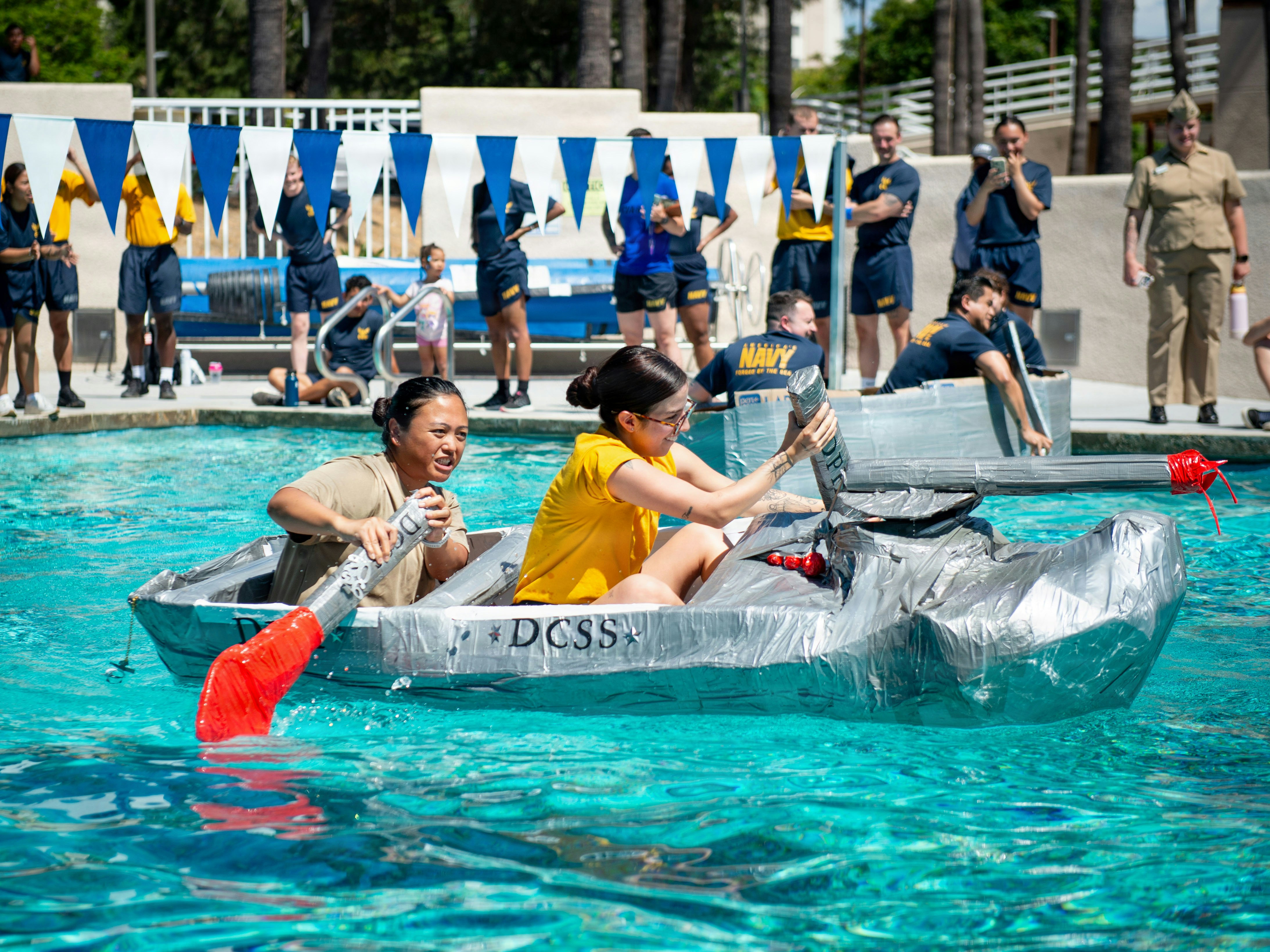 Sailors race a homemade cardboard boat in a swimming pool.