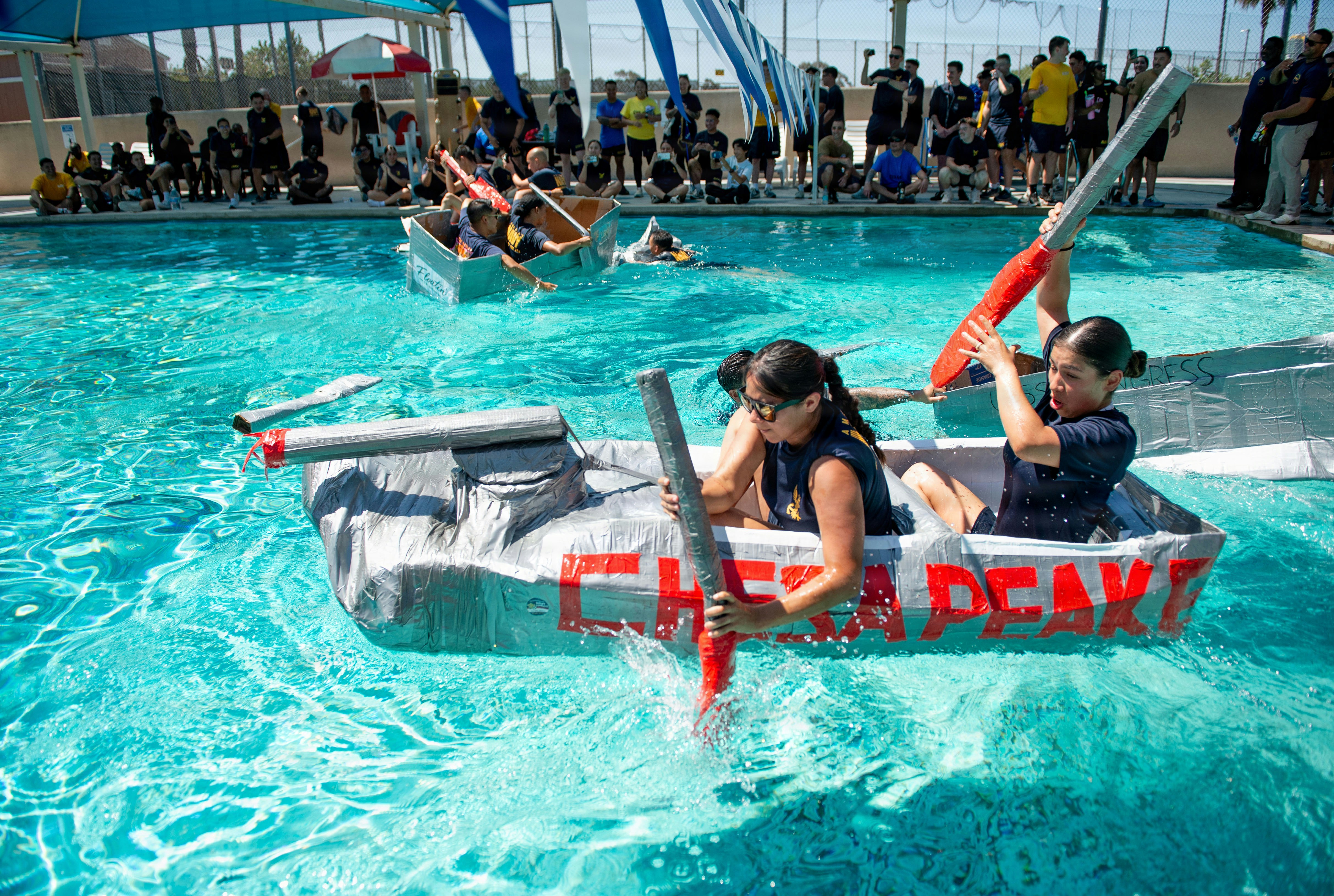 Two girls race homemade boats in a swimming pool.