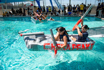 Two girls race homemade boats in a swimming pool.
