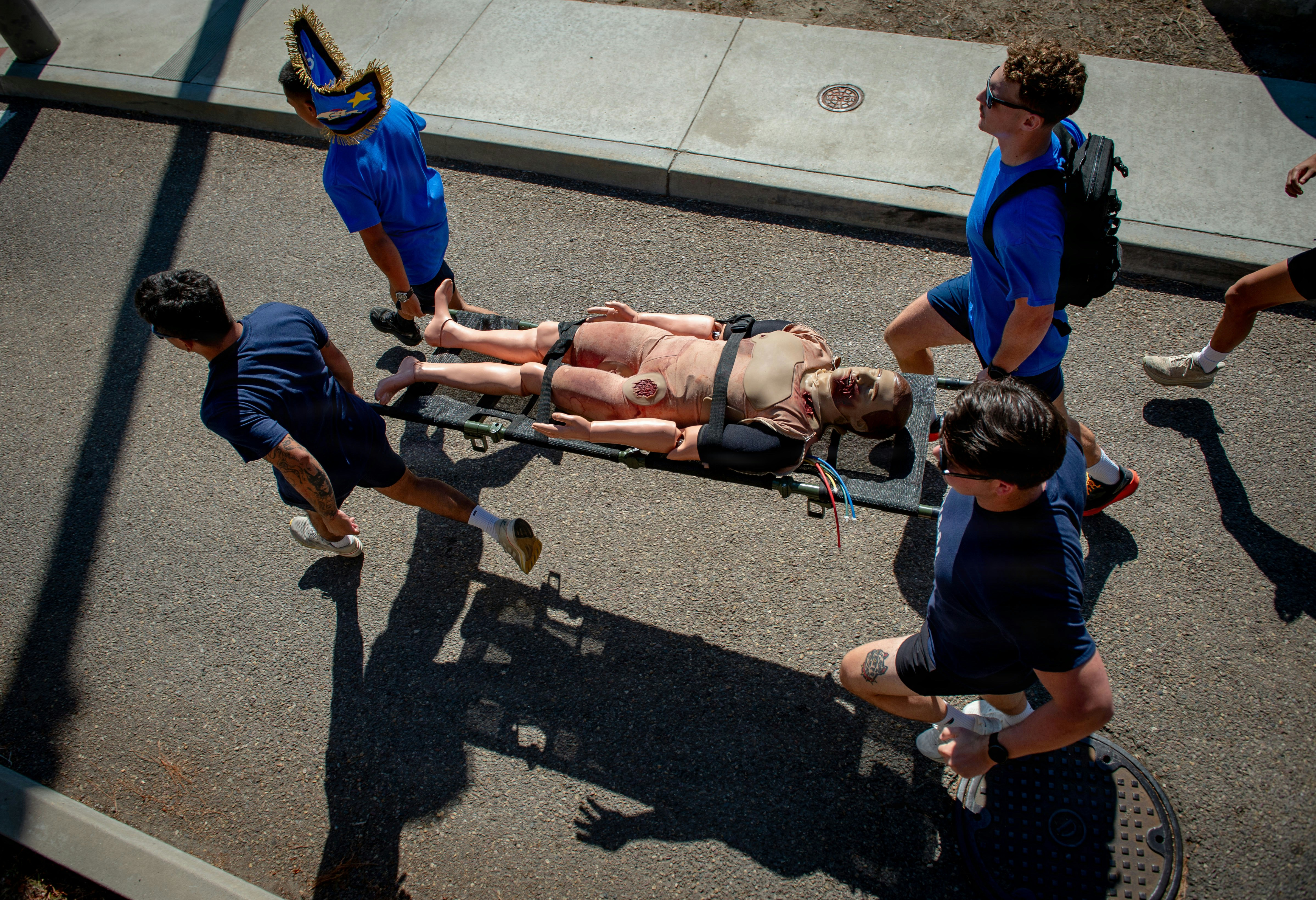 Four people carrying a mannequin on a stretcher outdoors.