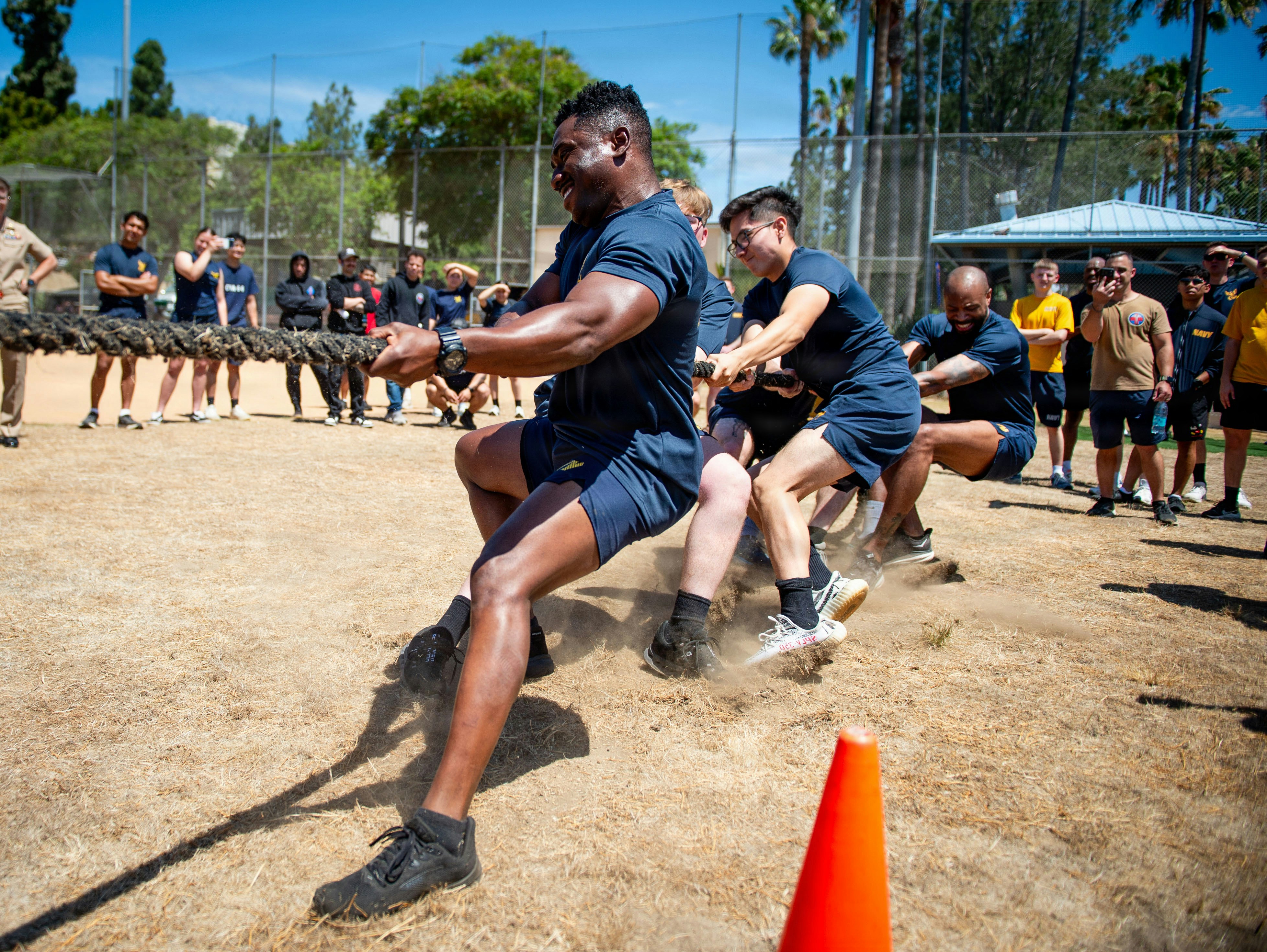 People vigorously play tug-of-war on a dusty field.