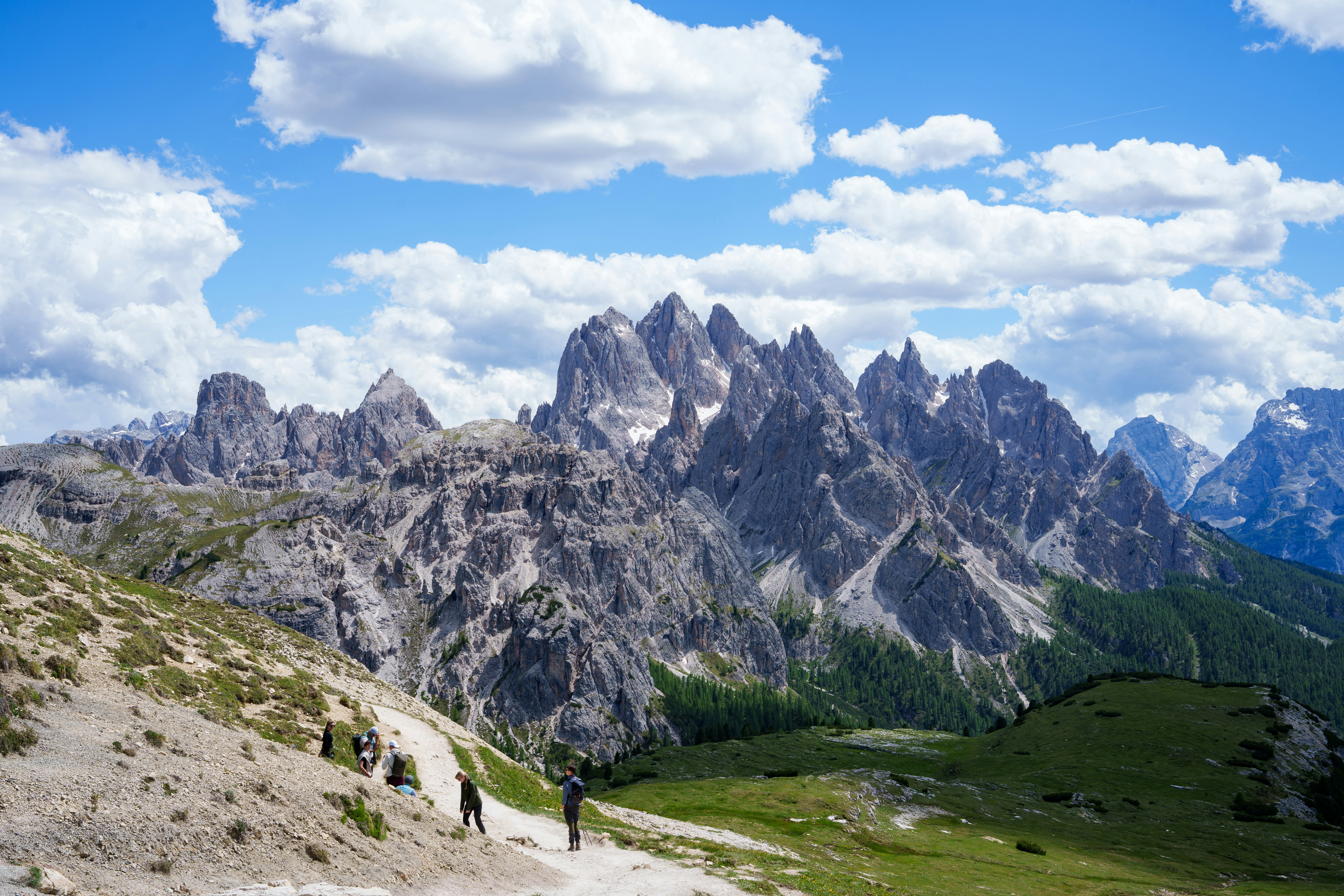 Hikers on a mountain path under a cloudy sky.