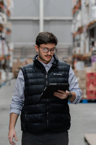 Man in vest using tablet in a warehouse.