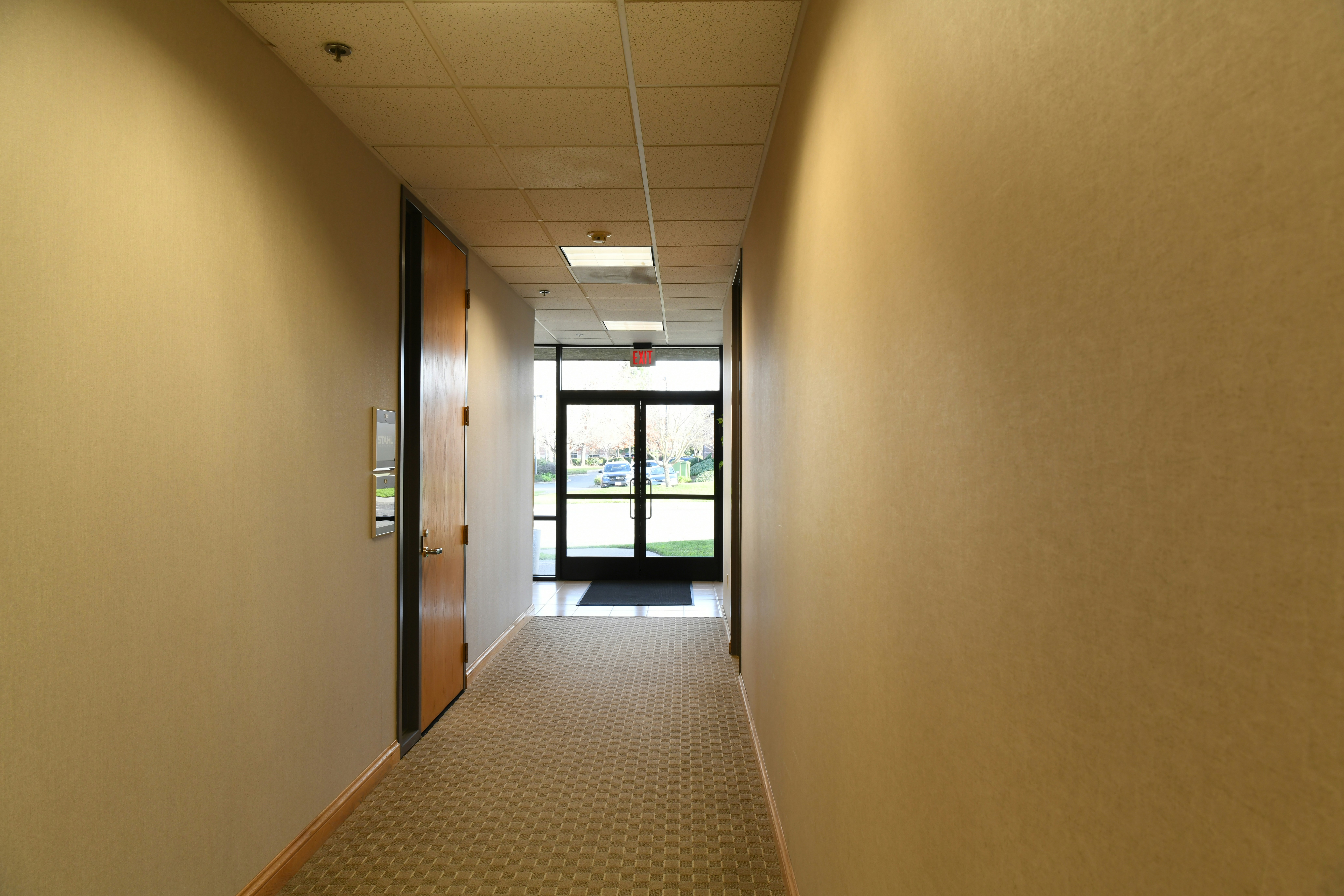 Long hallway with beige walls leading to an exit door.