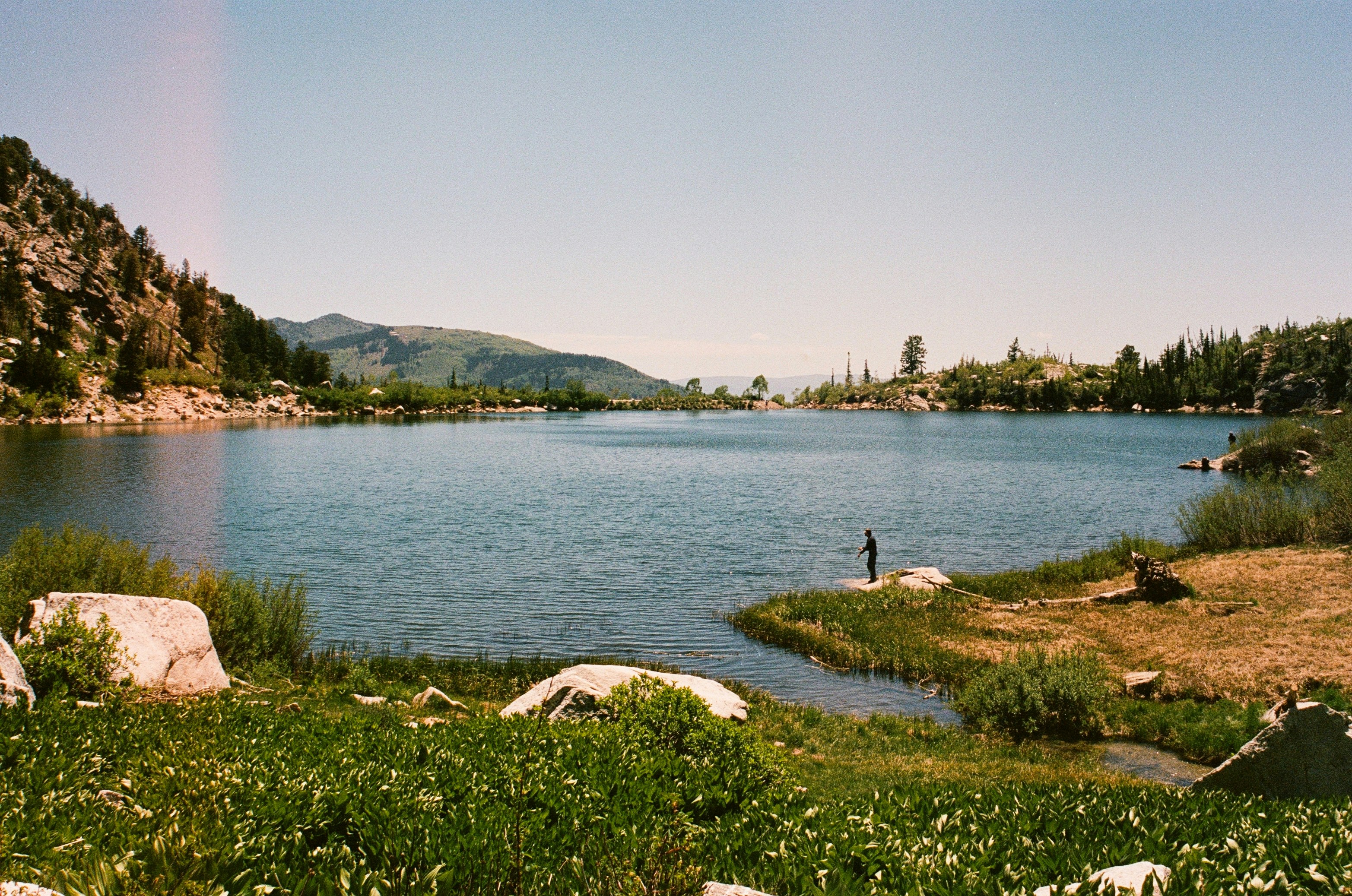 Scenic mountain lake with green shores and a person fishing.