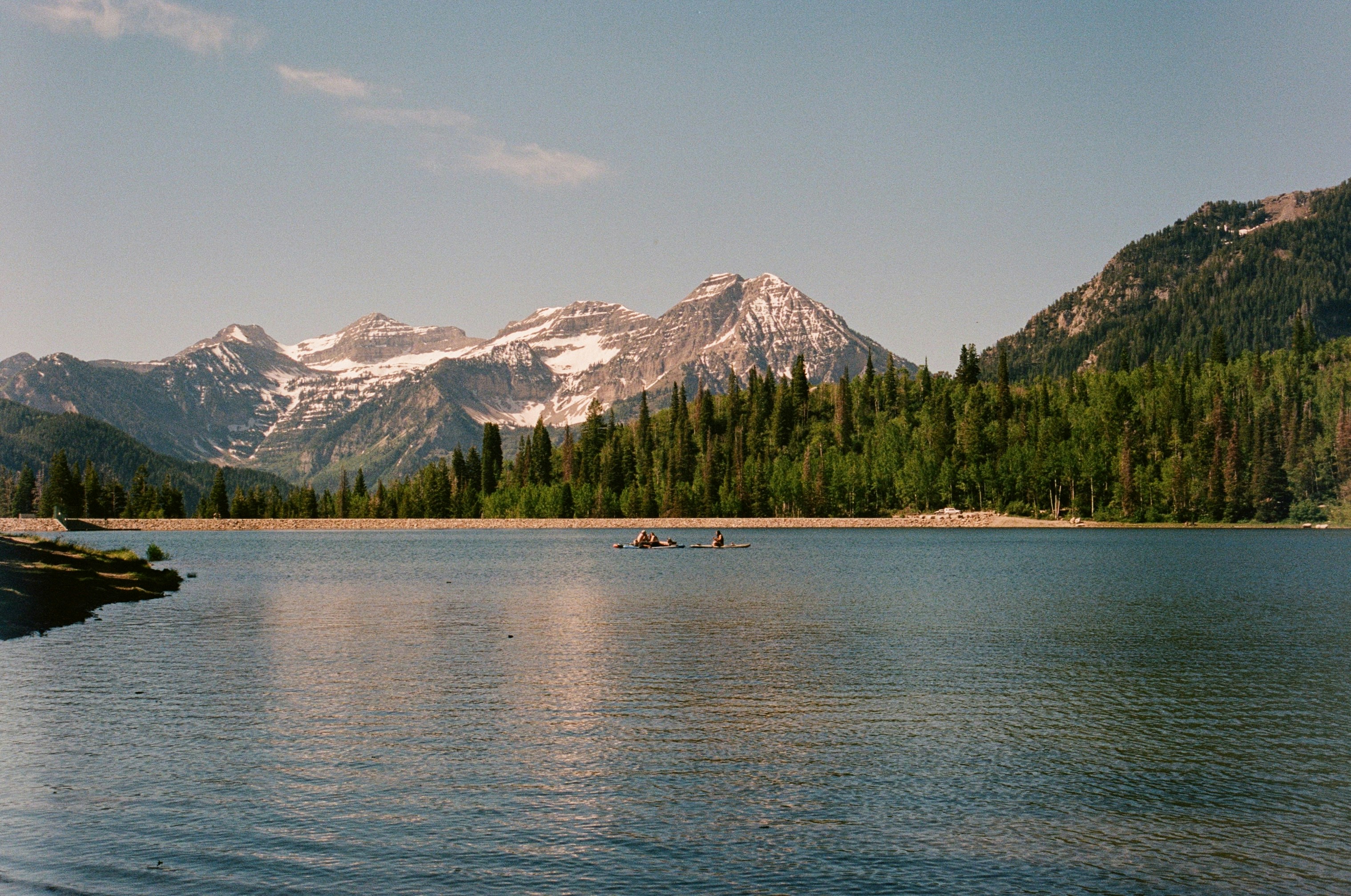 Majestic mountains overlook a tranquil lake with distant kayakers.