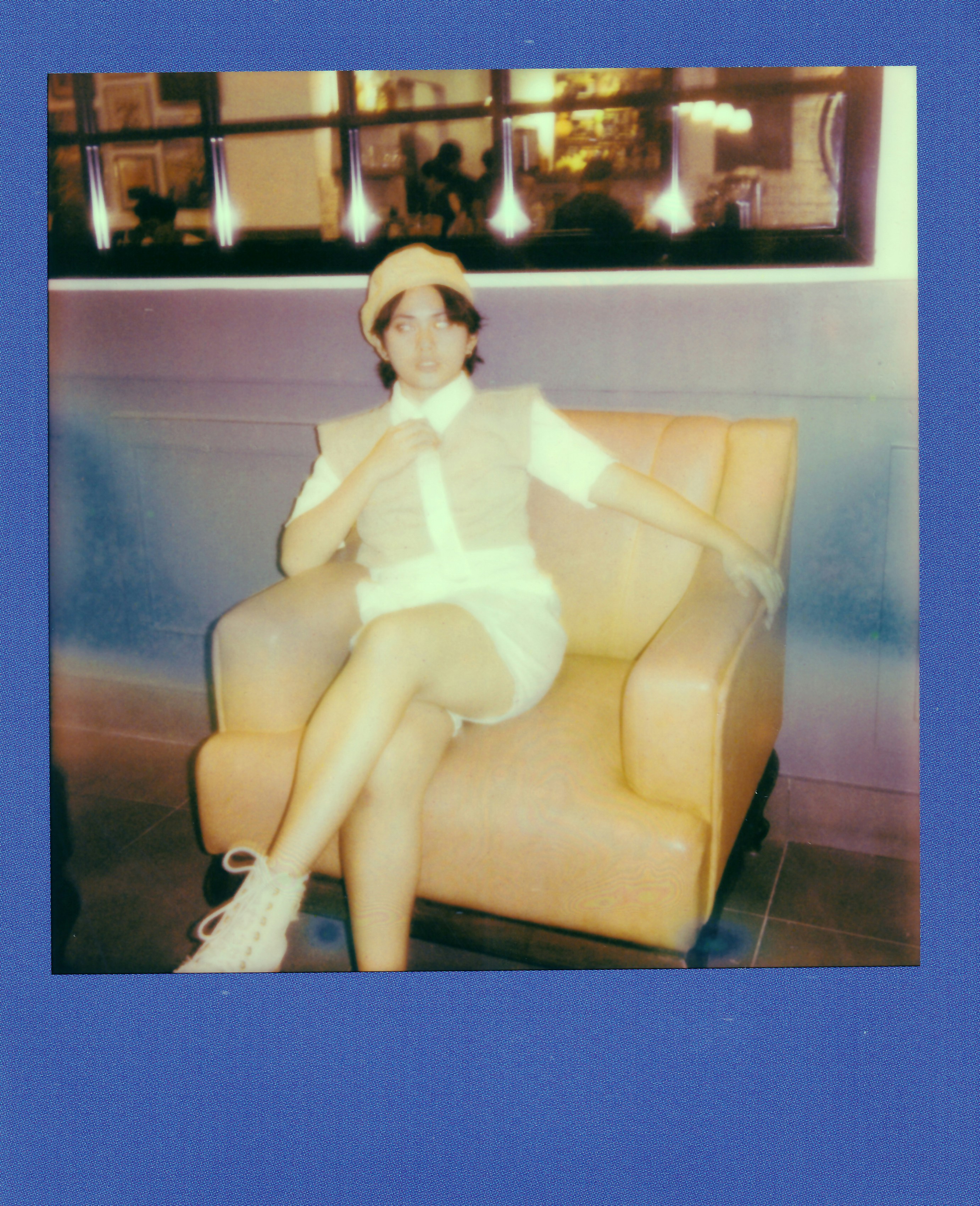 Person in light outfit and hat sits on yellow chair.