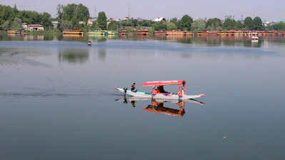 A person paddles a red-canopied boat across a calm lake.