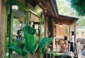 Green-framed cafe with outdoor patio and lush plants.