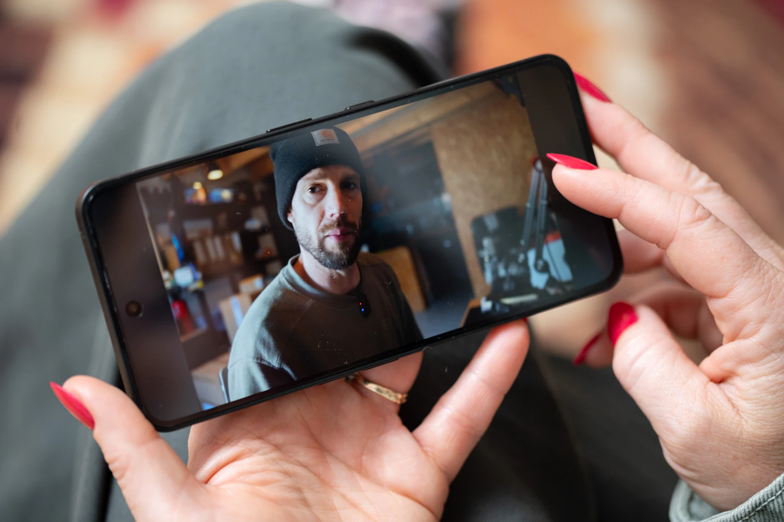 Hands holding a smartphone playing a video of a man talking to the camera