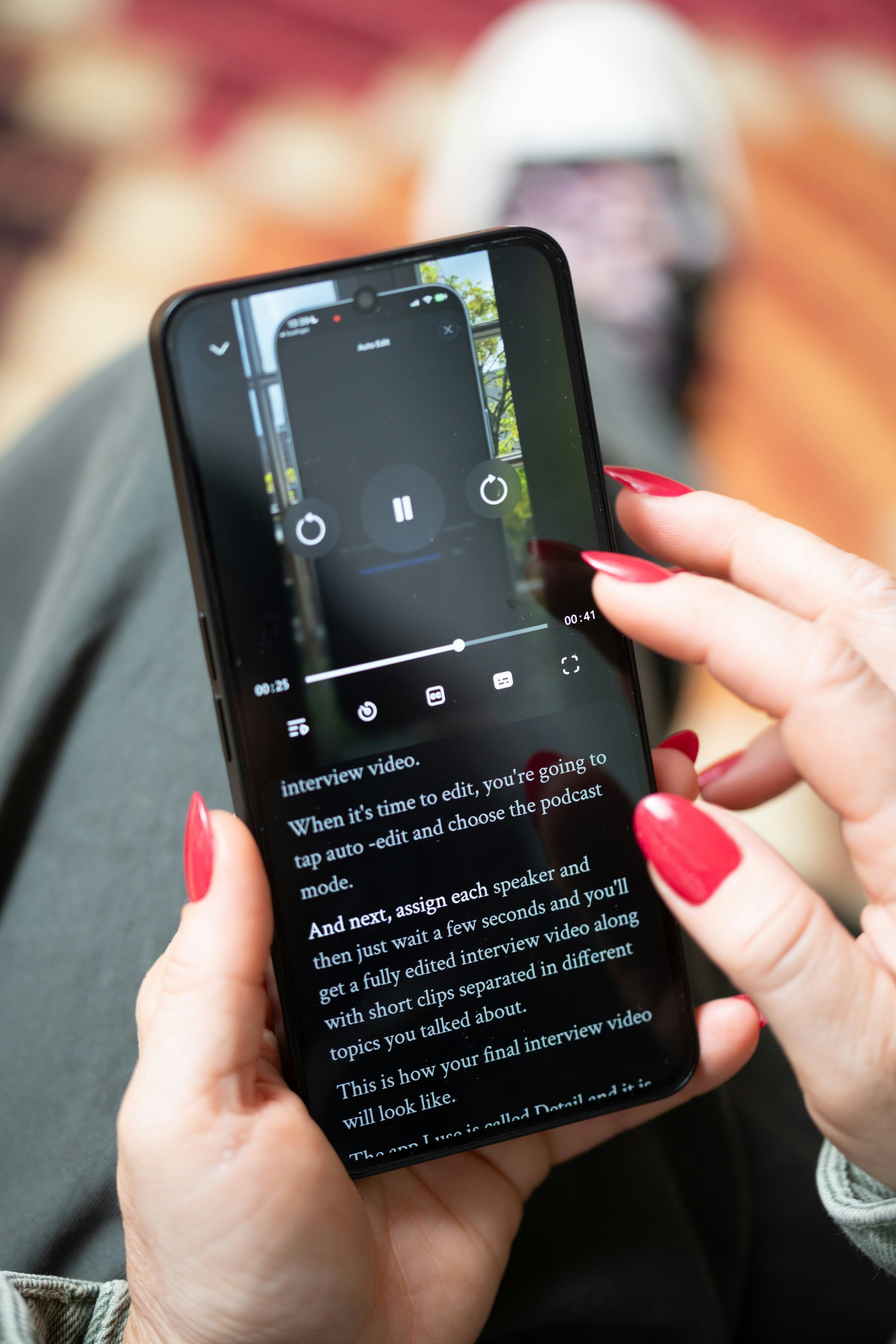 Tangan berpaku merah memegang smartphone yang menampilkan teks dan video.