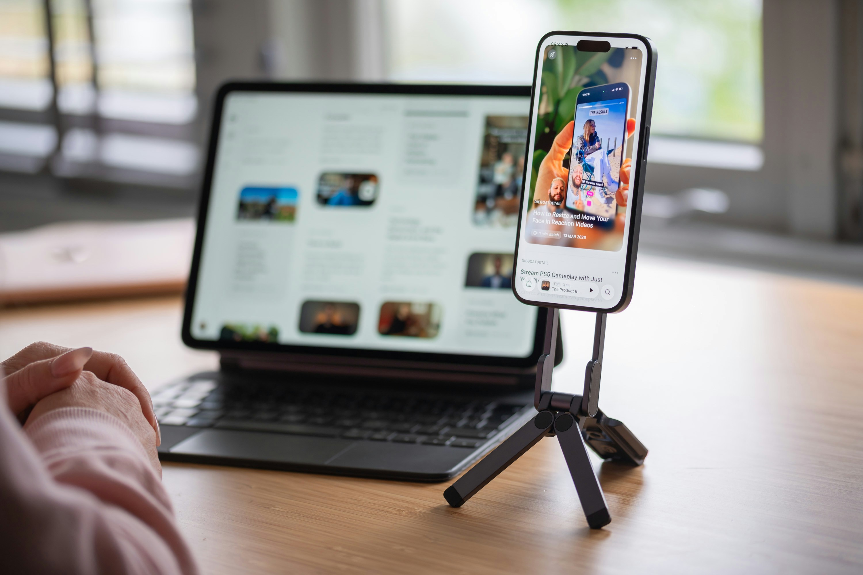 Person viewing smartphone on tripod next to a laptop.