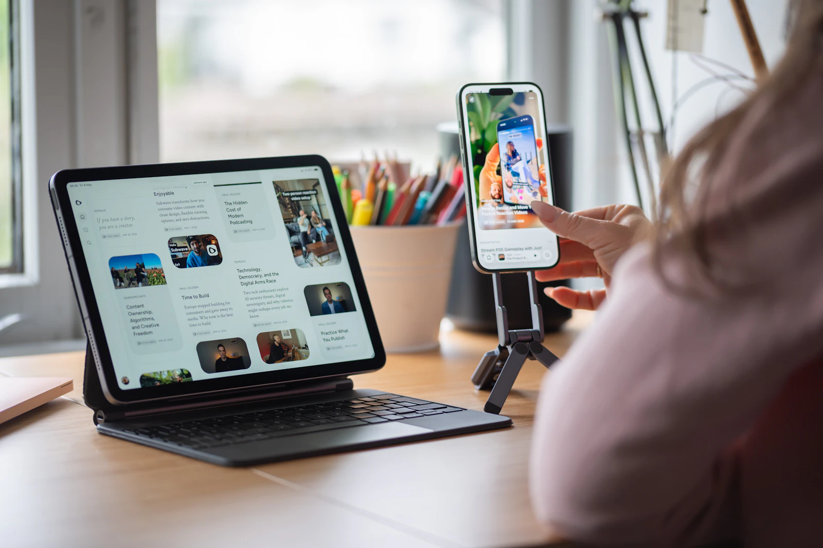 A person tapping a smartphone on a desk stand next to a tablet showing an article layout