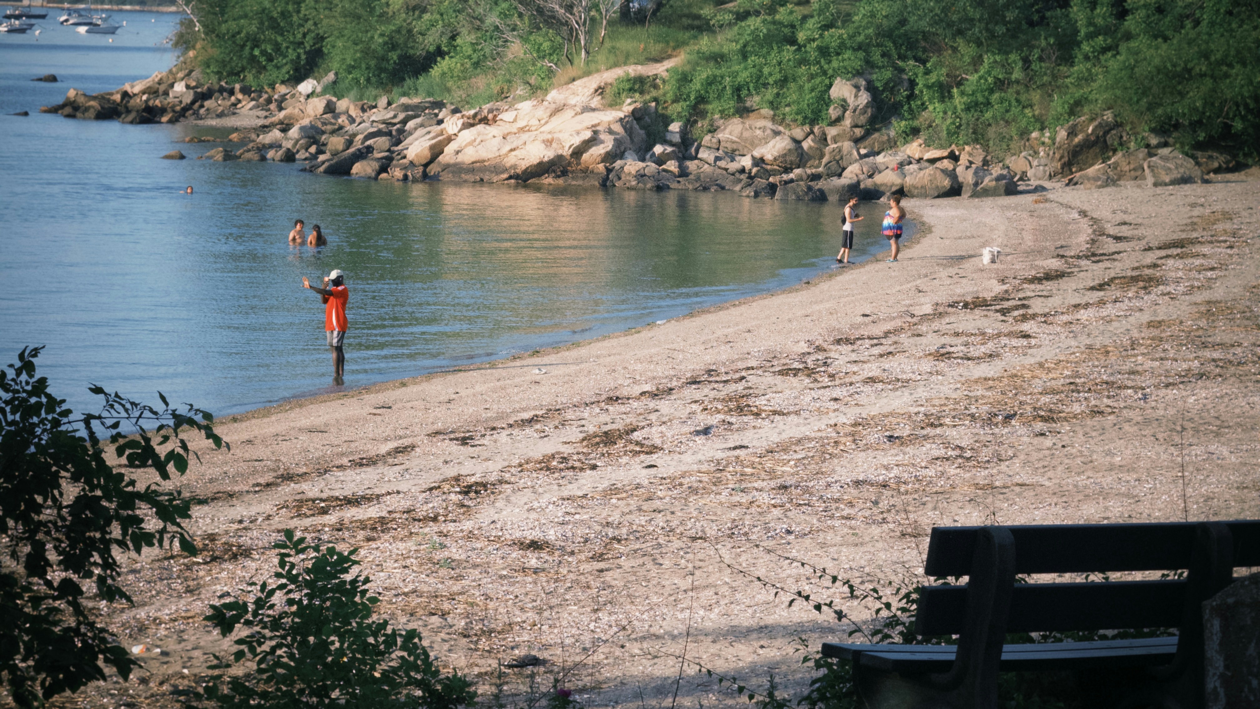 Person in orange wades in water near a sandy beach.