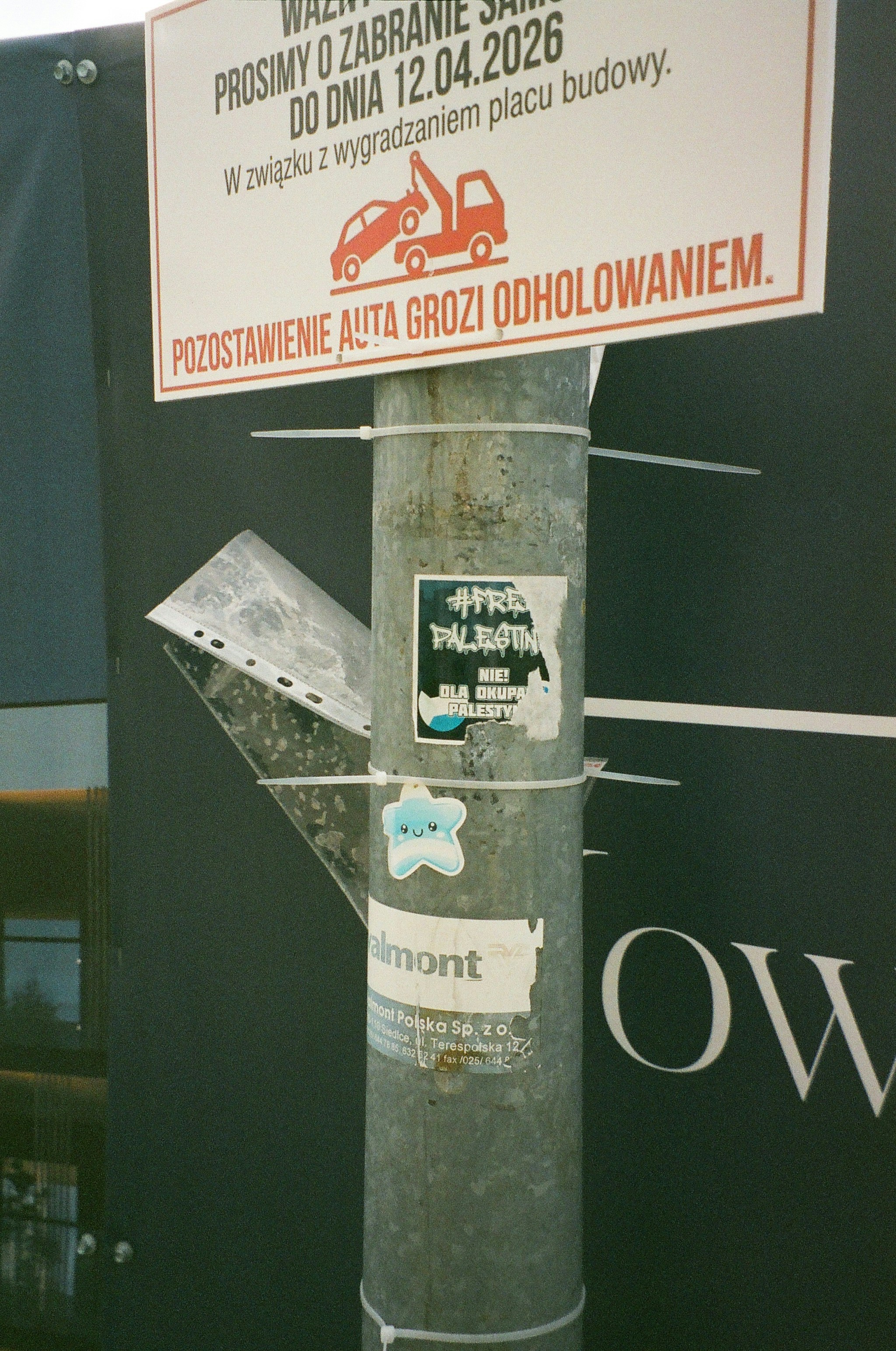 A metal pole with a towing warning sign and stickers