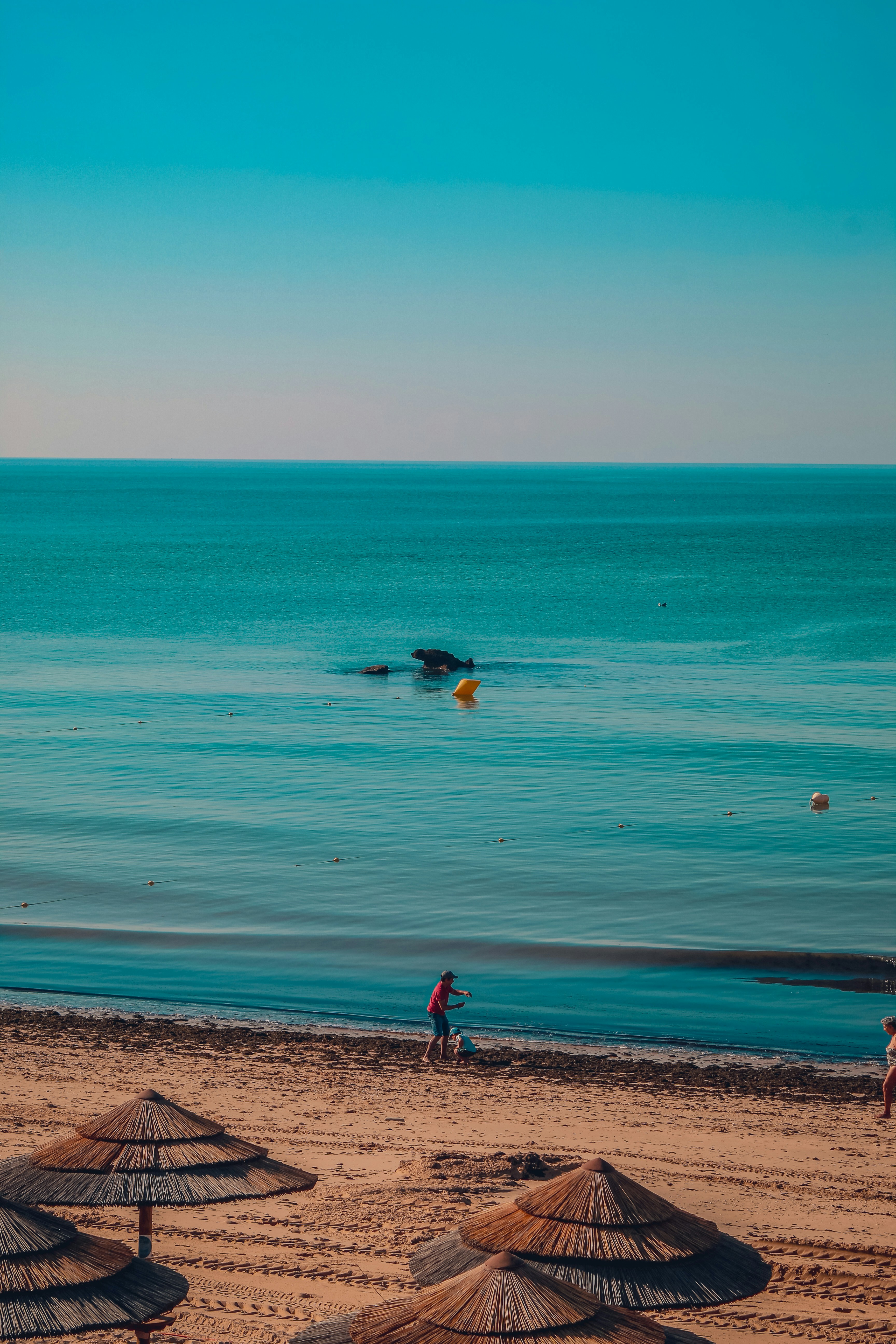 Uma praia de areia com guarda-sols, oceano calmo e céu limpo.