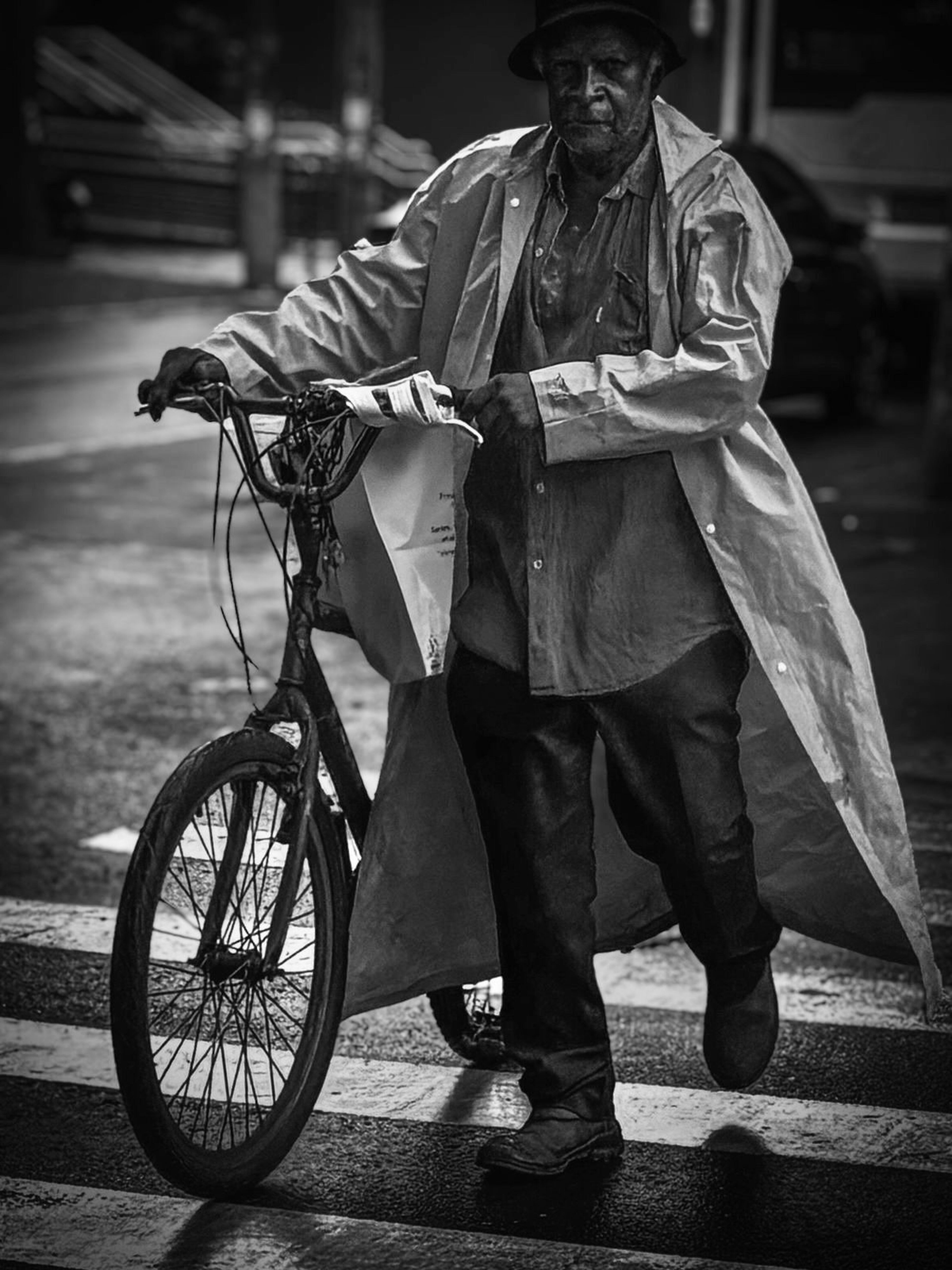 Man in raincoat walks bicycle on wet street