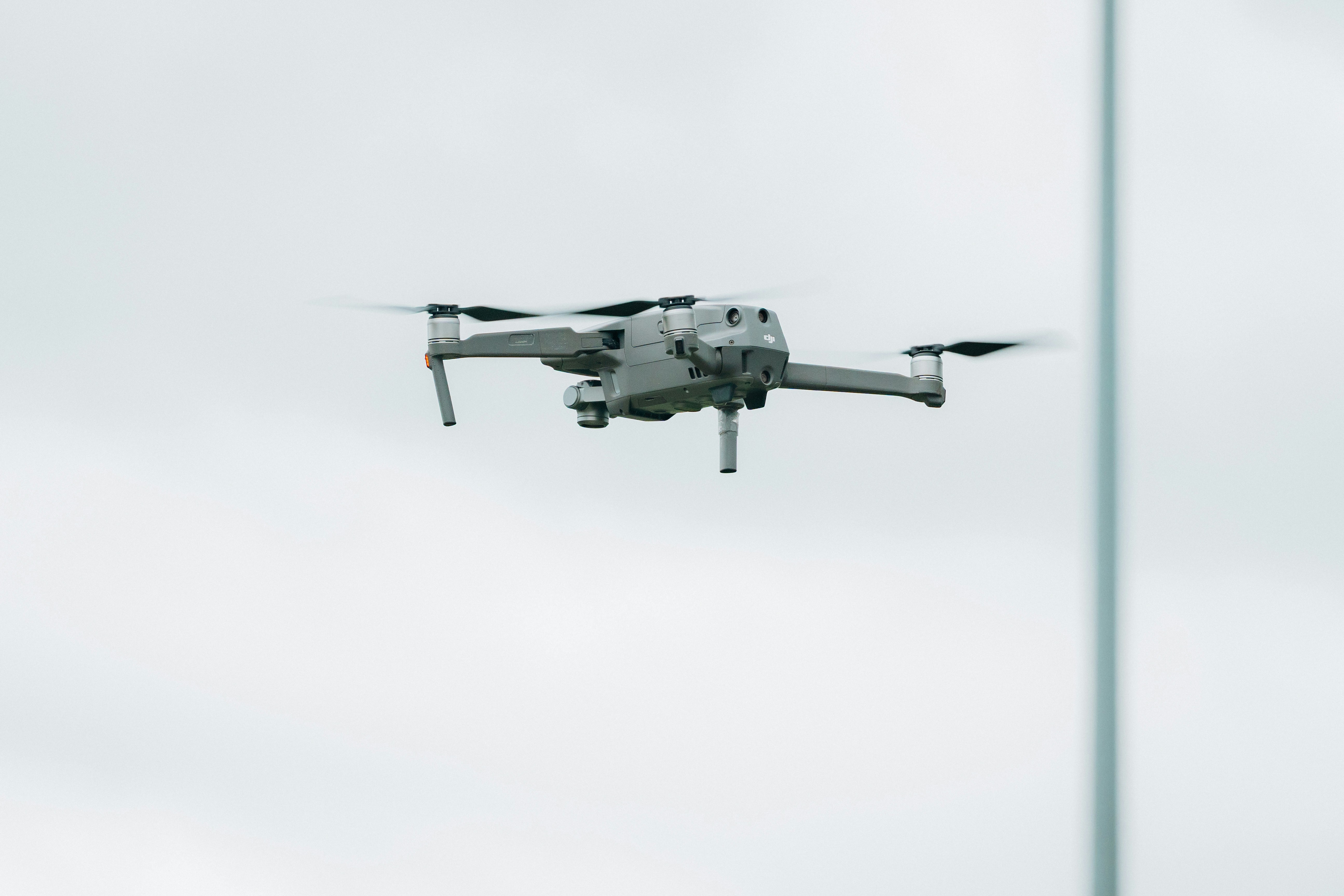 A gray drone flying in a cloudy sky.