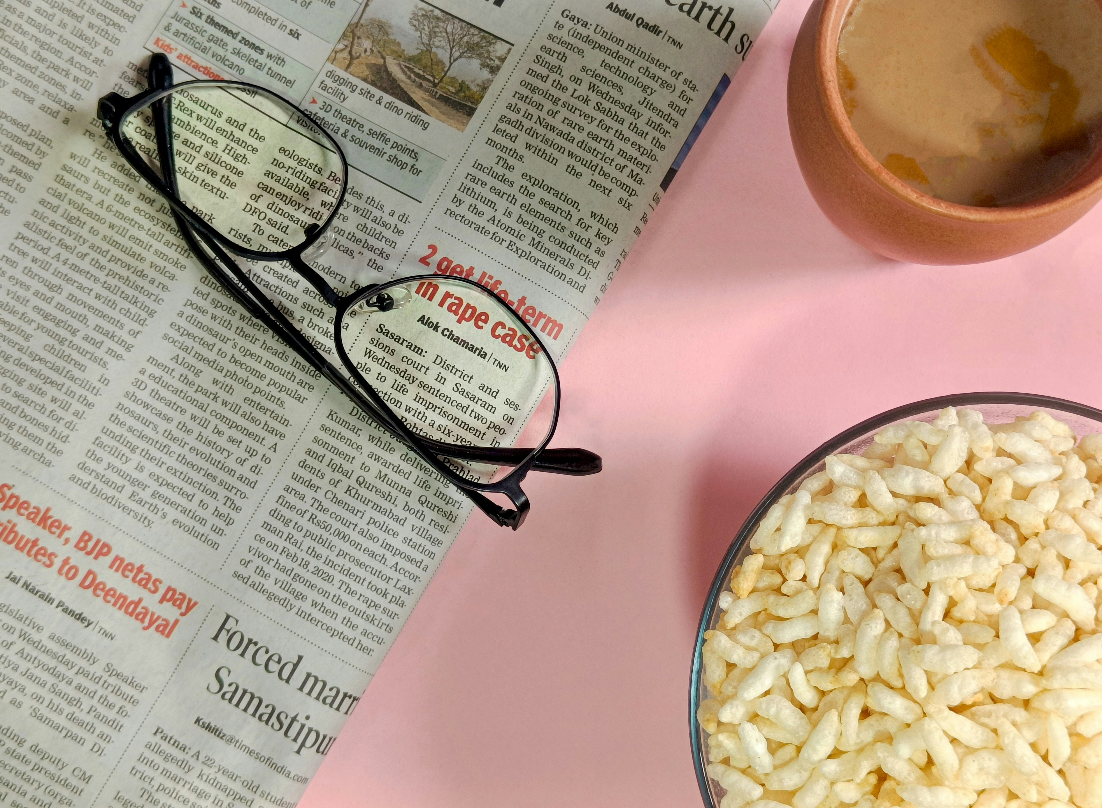 Newspaper, glasses, tea, and puffed rice on a pink background.