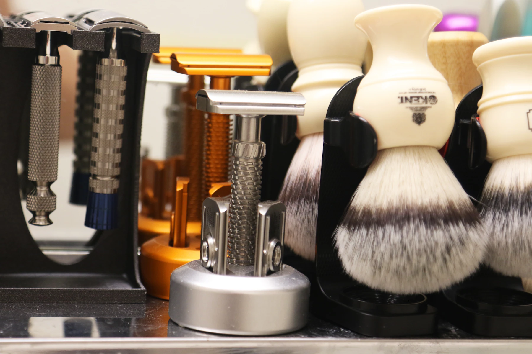 Safety razors hanging in stands beside white-handled shaving brushes on a shelf