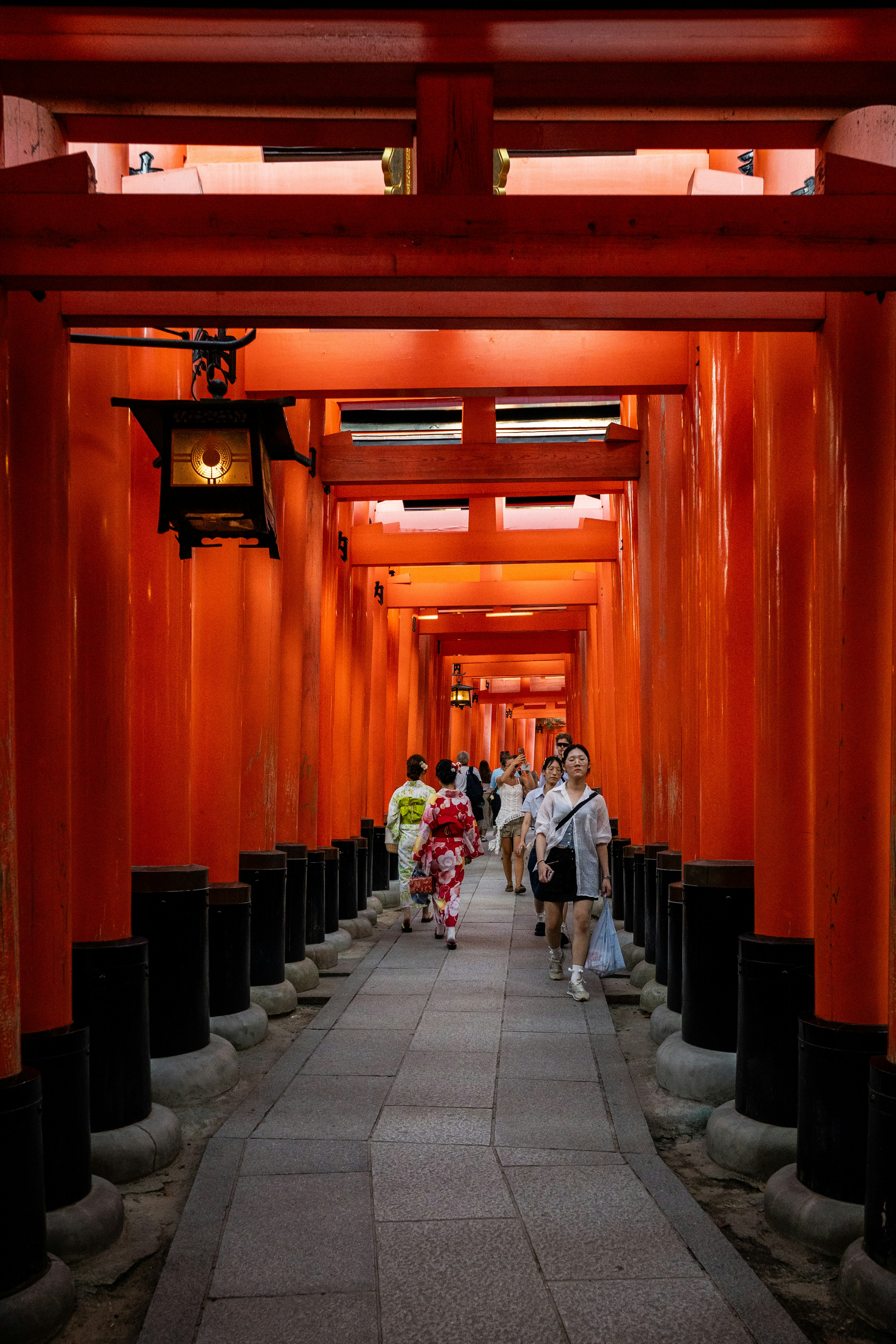 People walking through a tunnel of red japanese torii gates.