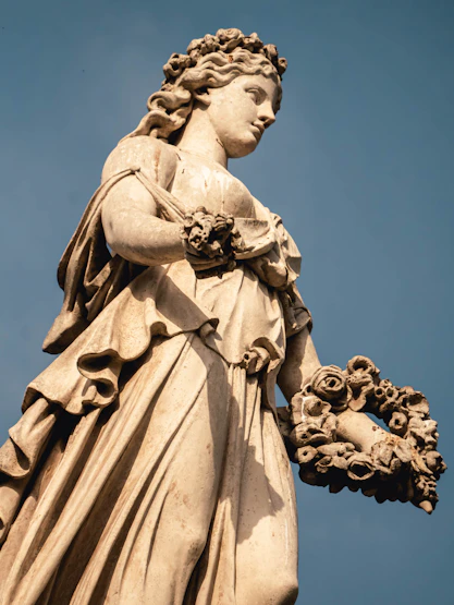 Classical marble statue of a woman holding a floral wreath.