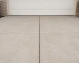 A concrete driveway in front of a white garage door.