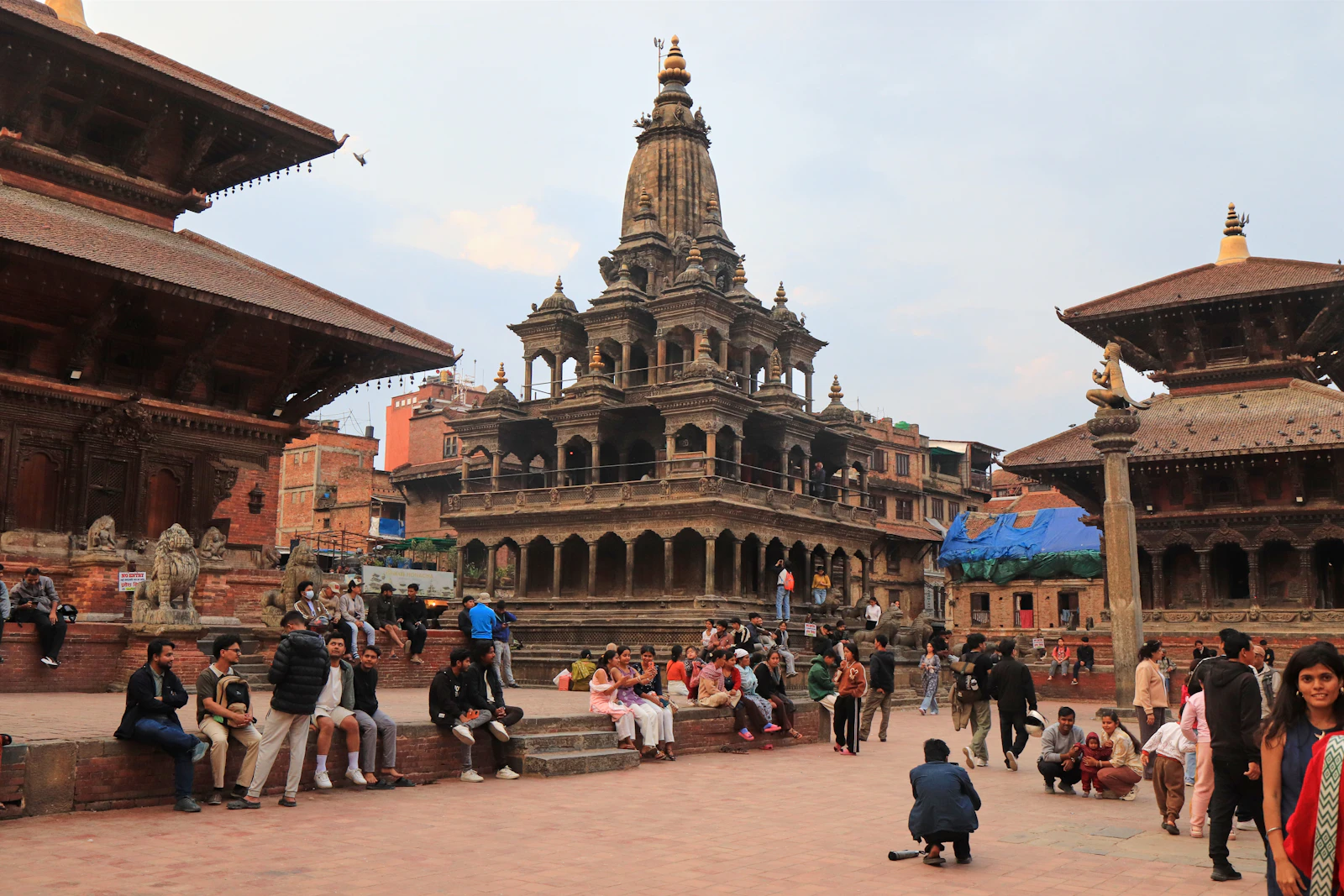 Patan Durbar Square in the Kathmandu valley, the stone Krishna Mandir between carved pagoda temples, people resting on the steps