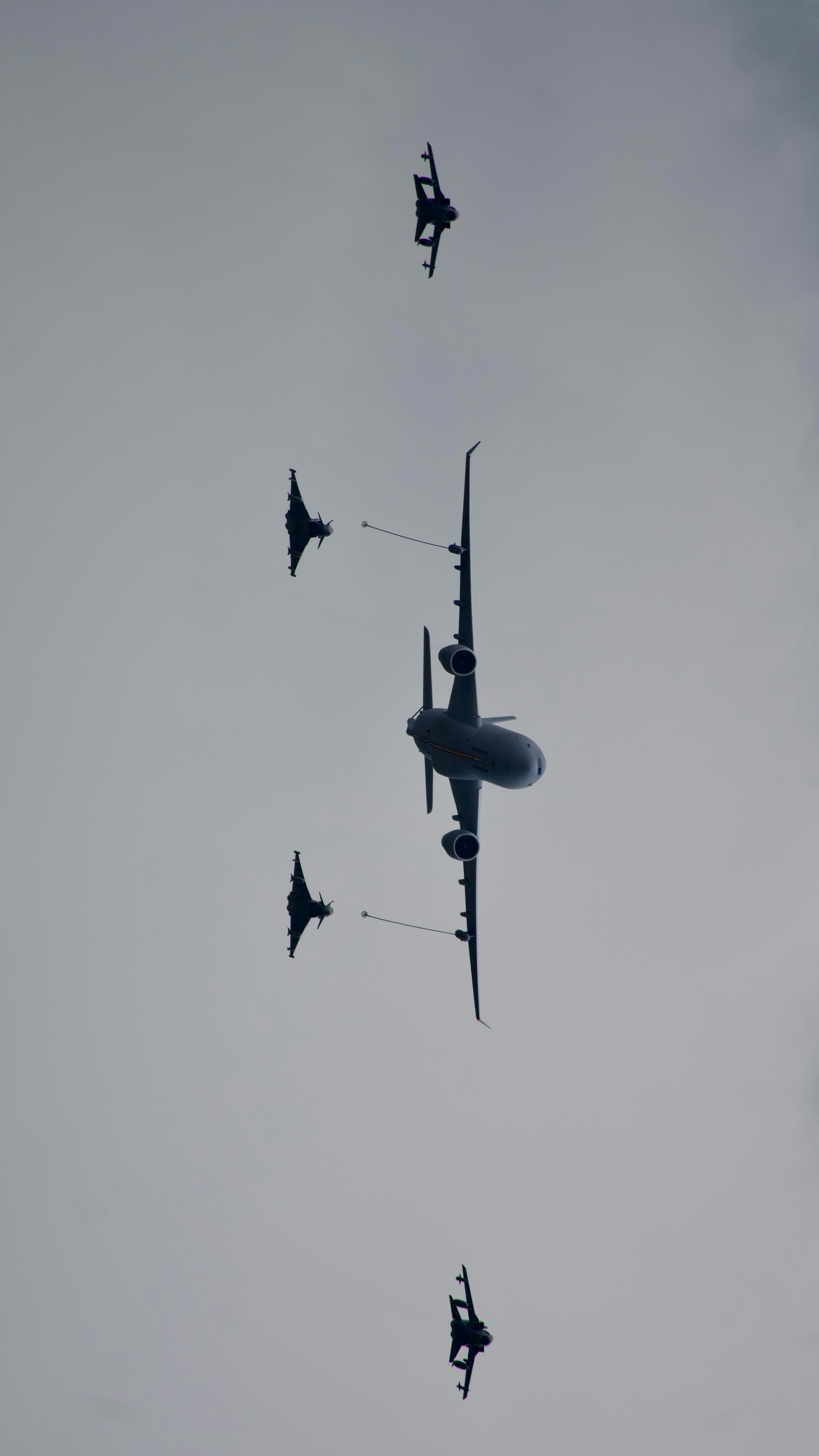 Military aircraft formation with fighter jets refueling in cloudy sky.