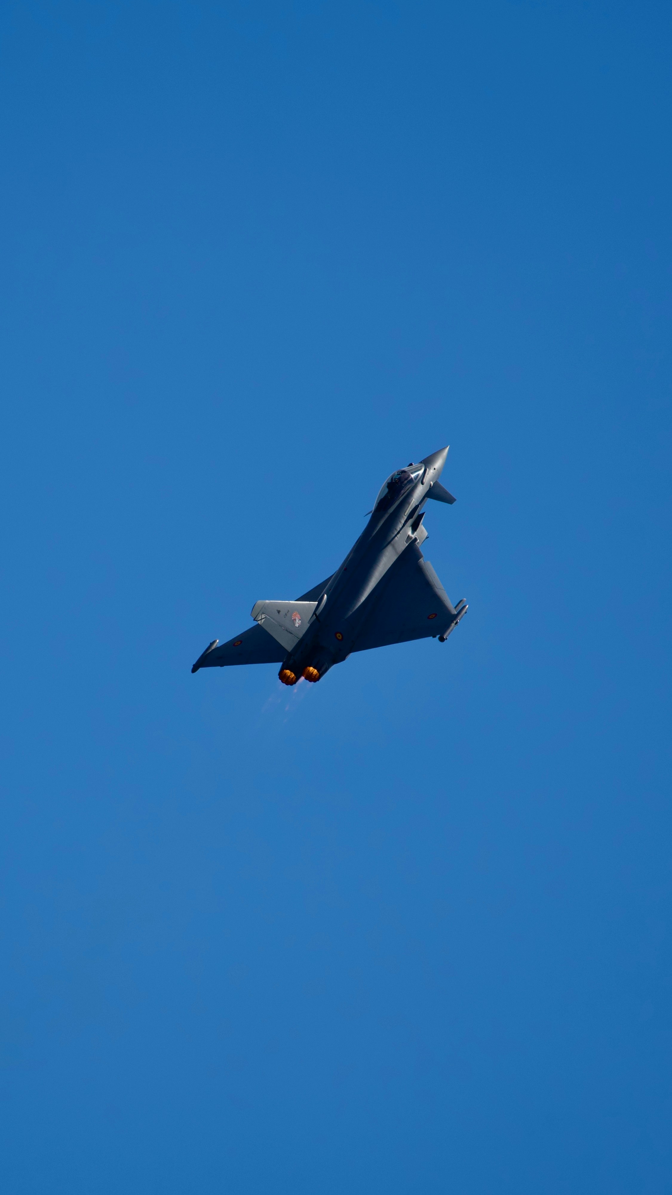 A fighter jet flying with afterburners against a blue sky.