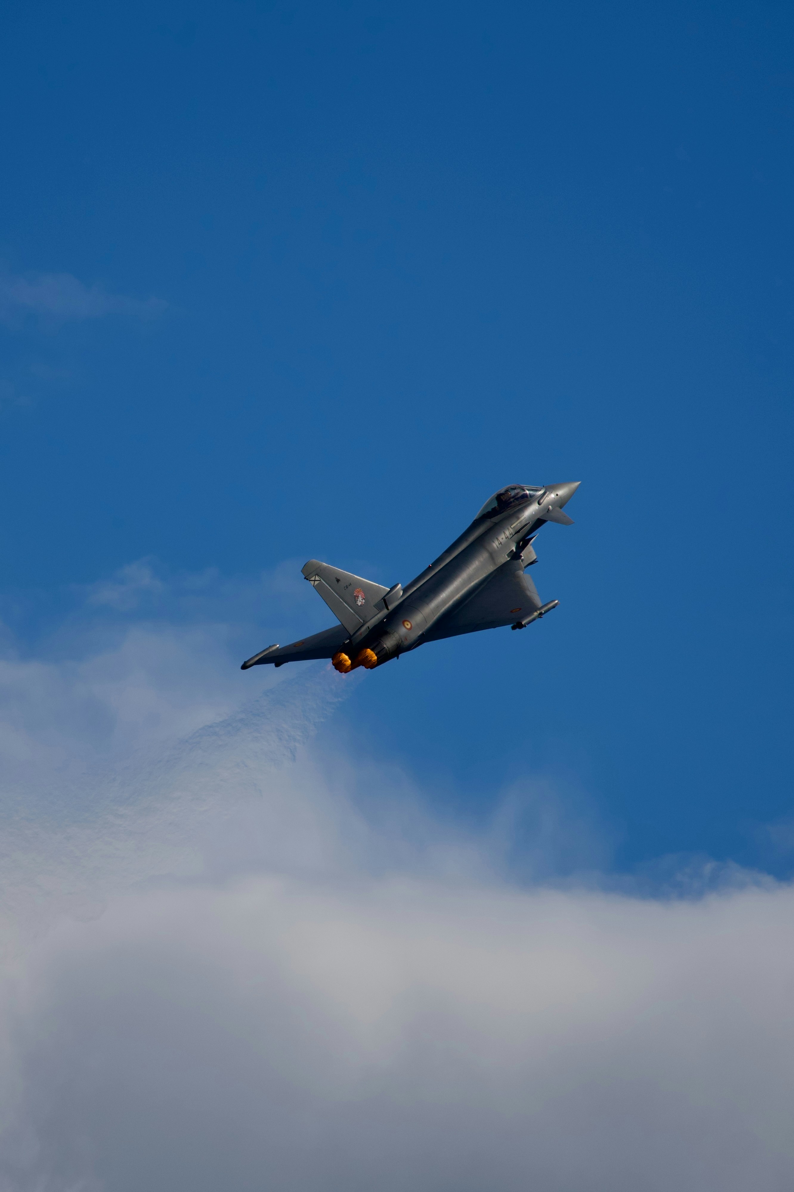 Fighter jet with glowing engines soaring through a blue sky.