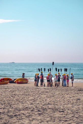 Kayakers gather on a sandy beach with paddles and boats