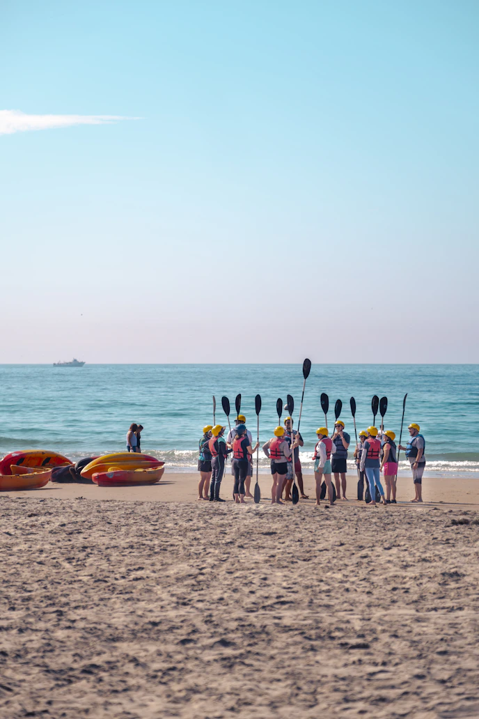 Kayakers gather on a sandy beach with paddles and boats