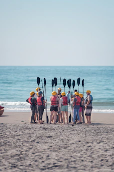 Group of kayakers with paddles gathered on a sandy beach