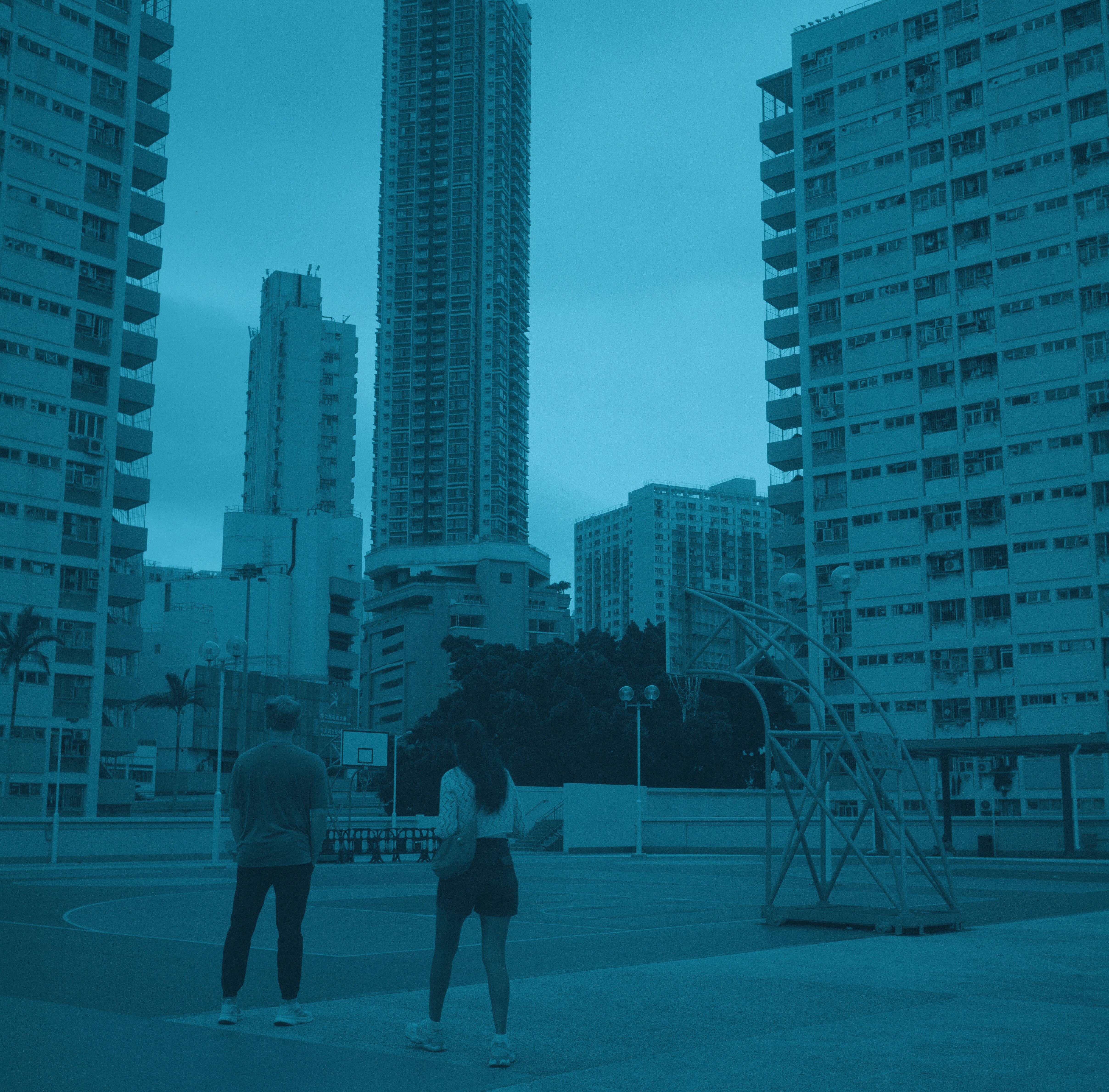 Two people stand on a basketball court with city buildings.