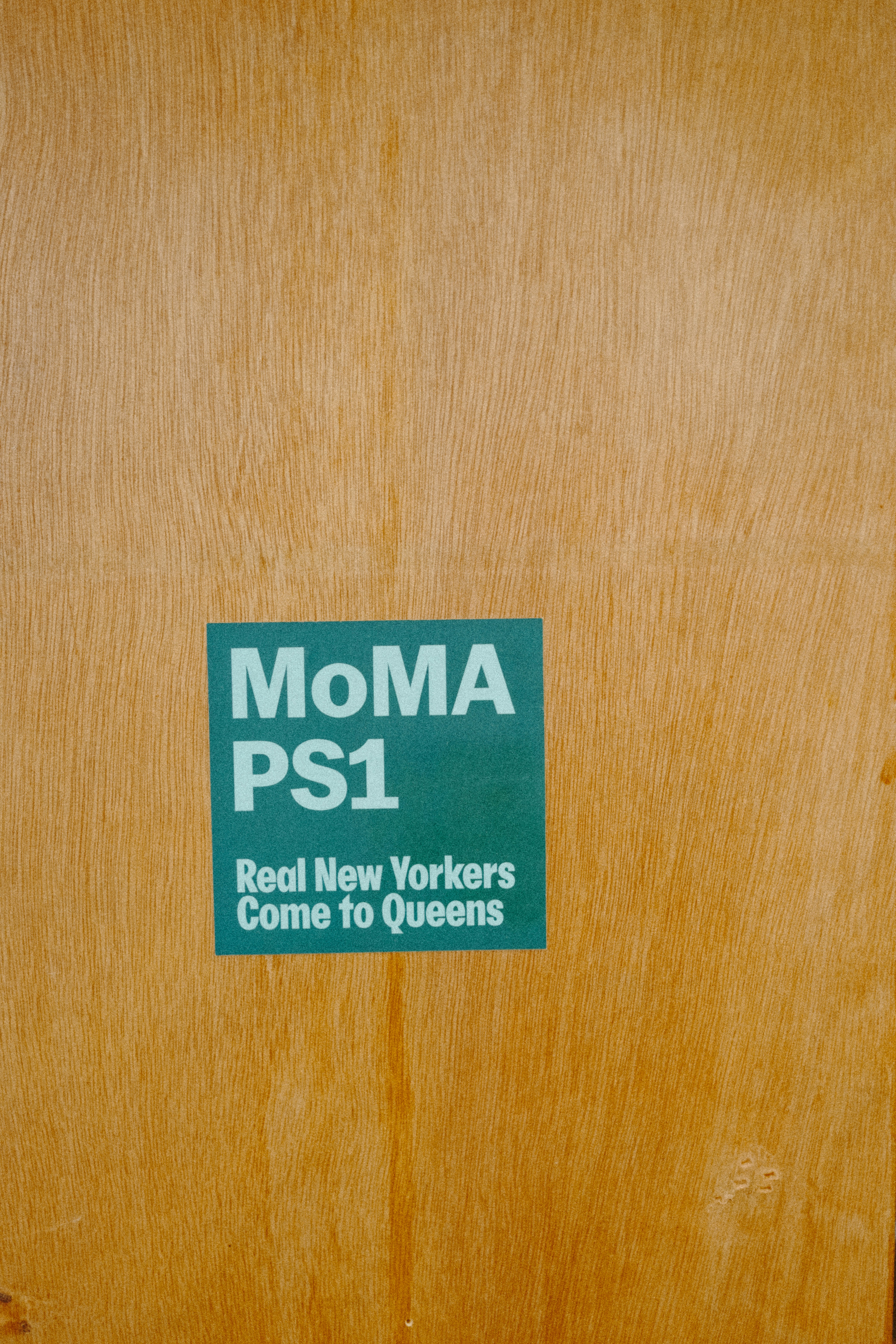 Ein grüner Moma PS1-Aufkleber an einer Holzwand