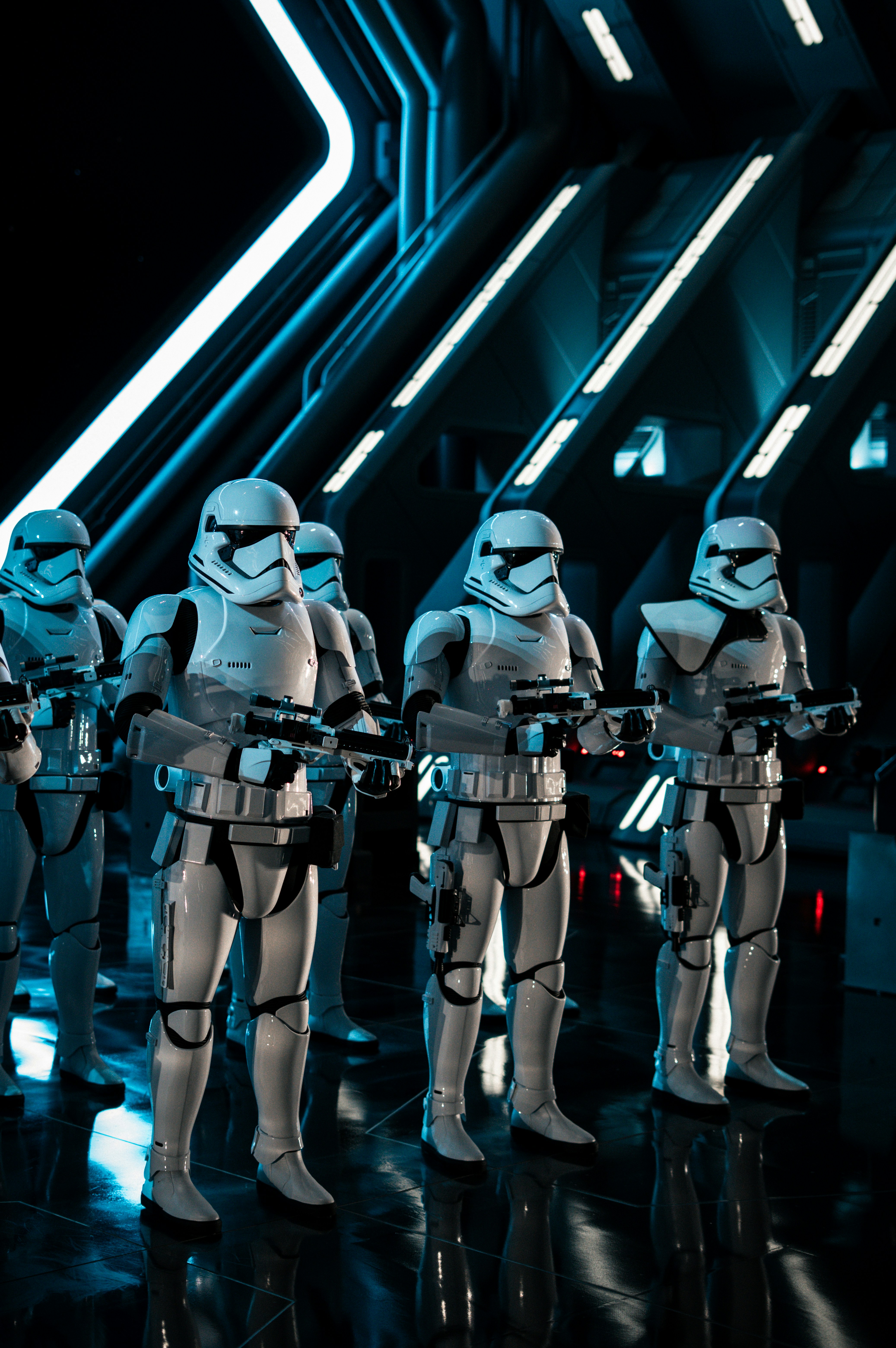 Beberapa stormtrooper berdiri di koridor futuristik yang gelap dan bercahaya biru.