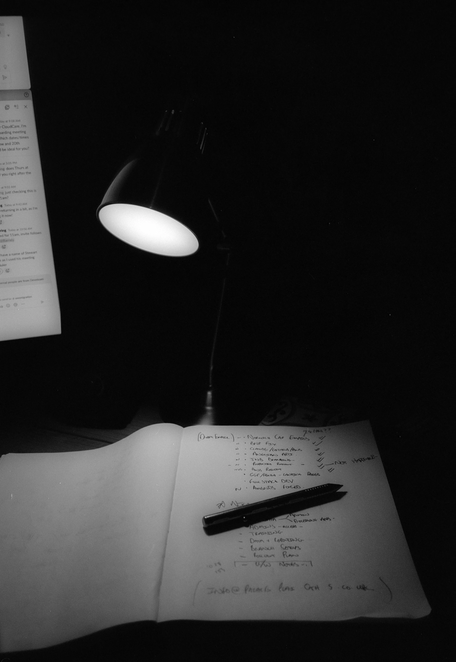 A lit desk lamp illuminates a notebook and pen