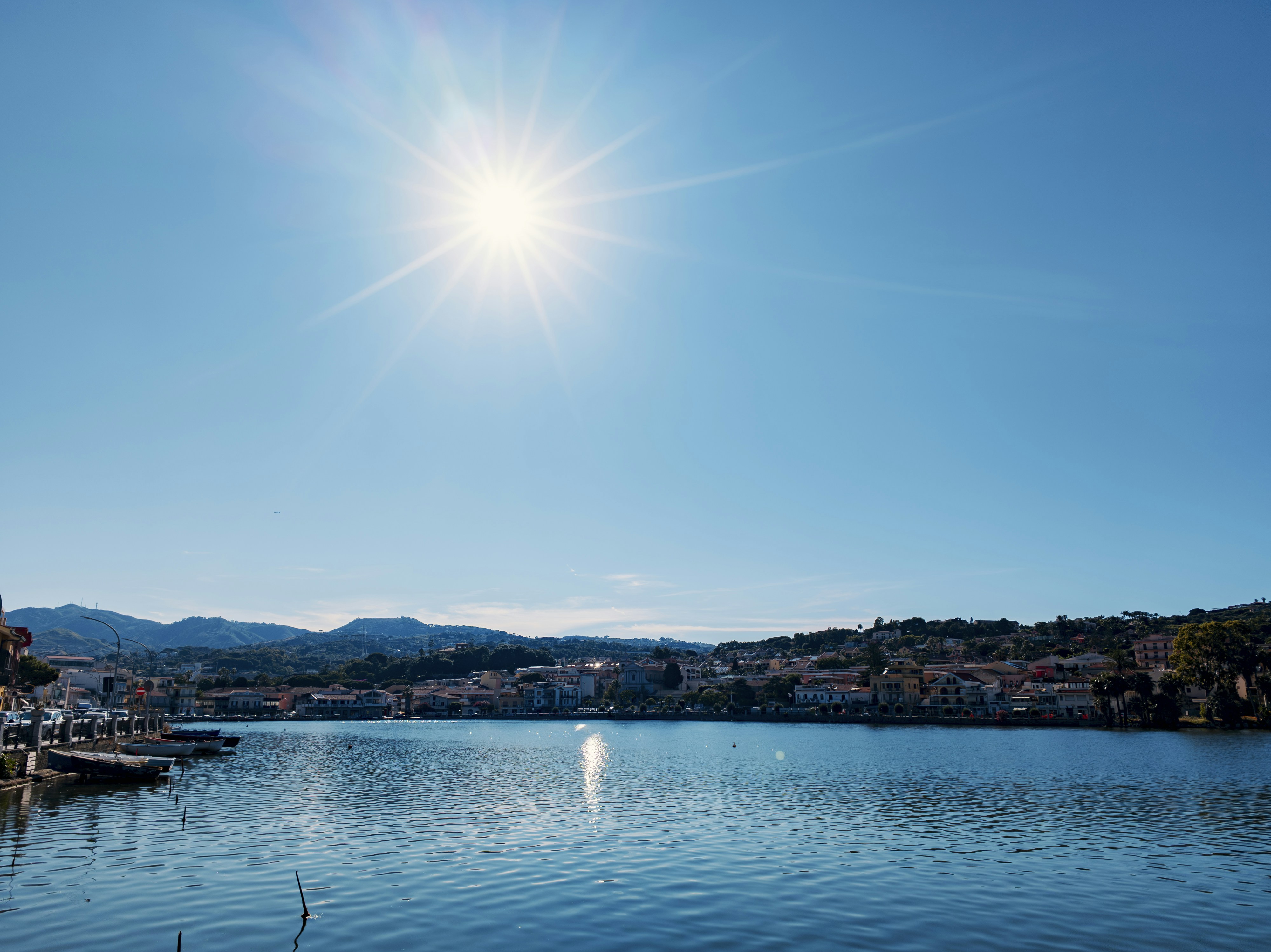 Sole splendente su una baia serena, una città lontana e montagne.