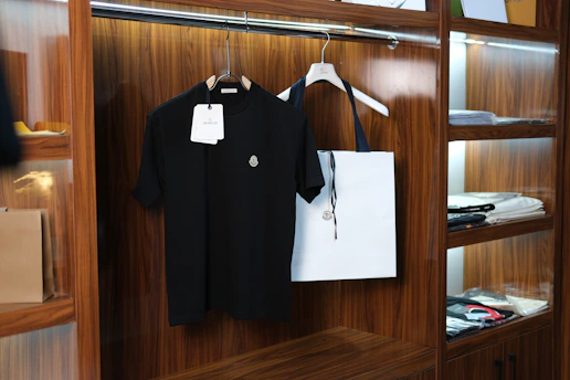 Black t-shirt and white tote bag hanging in wooden closet
