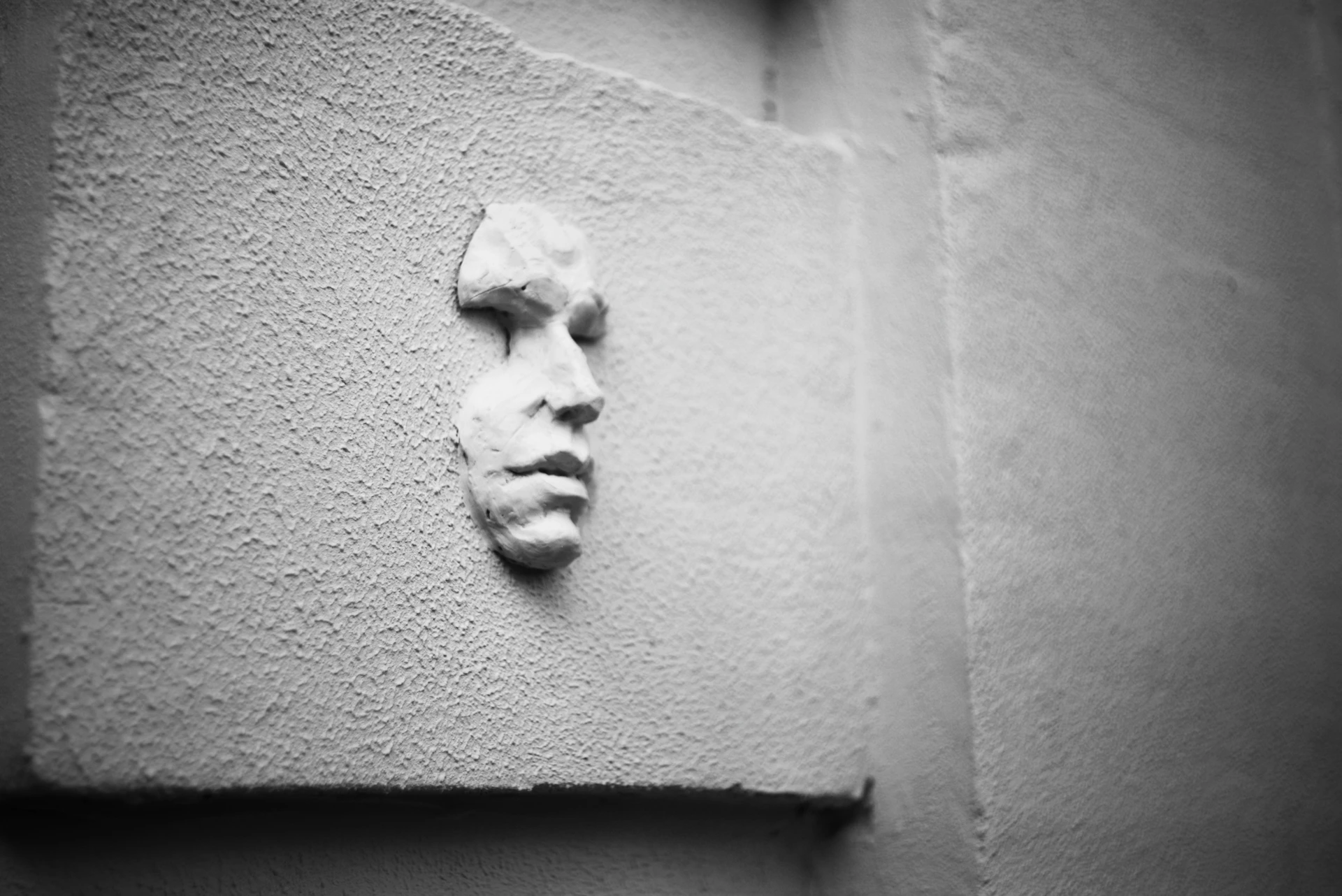 A sculpted human face emerges from a textured wall.