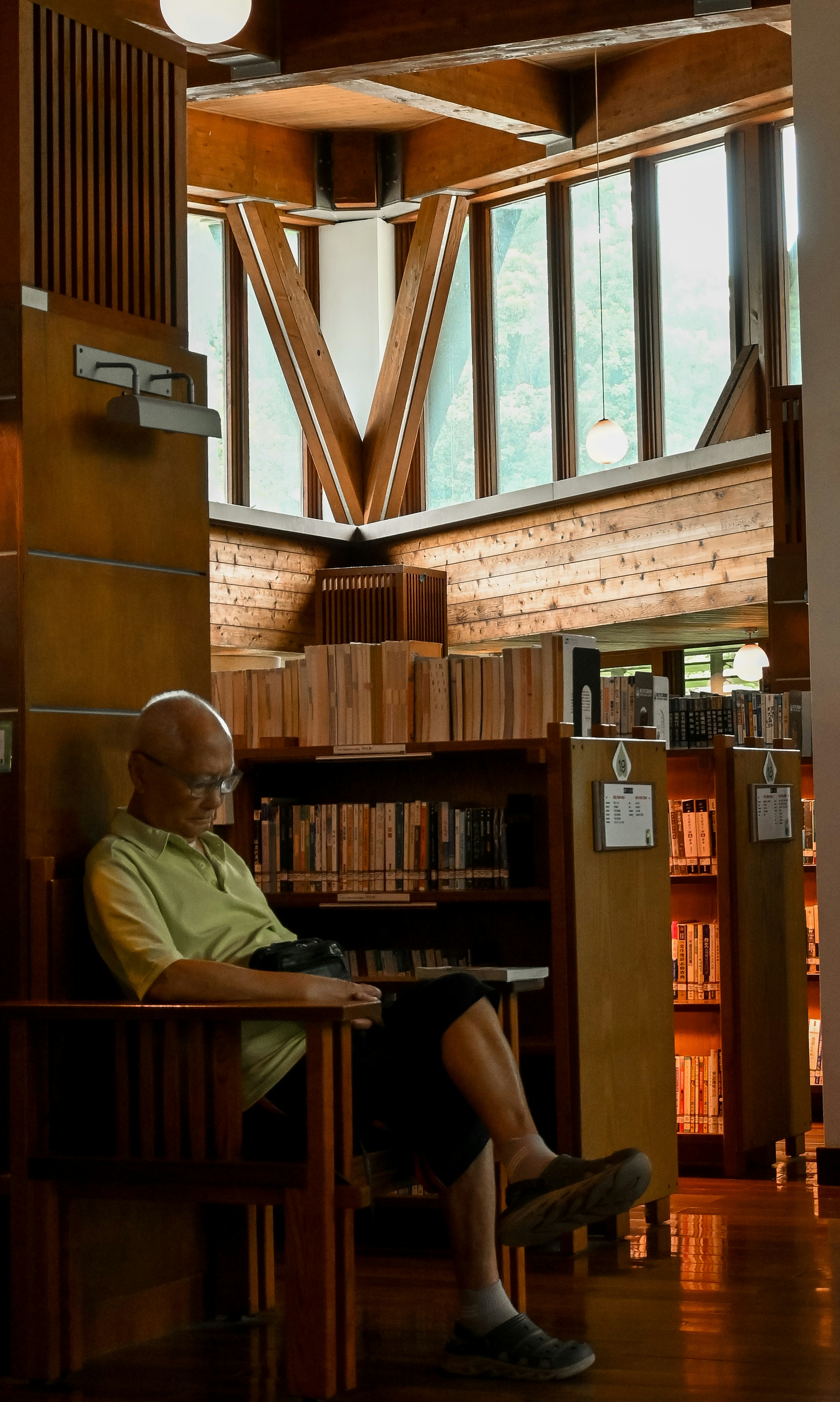A man reads quietly in a library with wooden bookshelves.