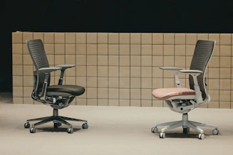 Two ergonomic office chairs, dark and light, facing each other.