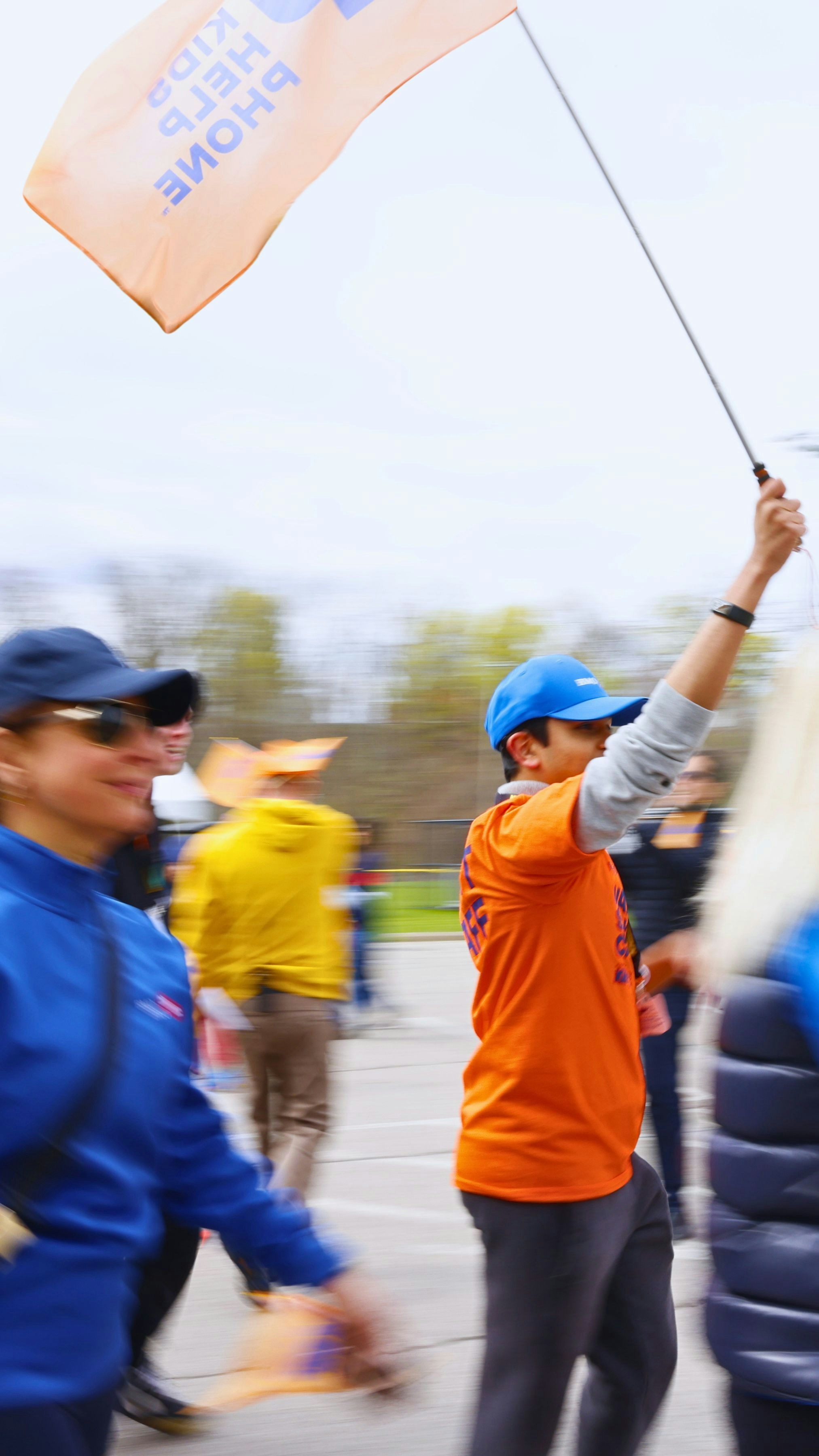 Orang-orang berjalan di luar ruangan, salah satunya memegang bendera "anak-anak membantu telepon".