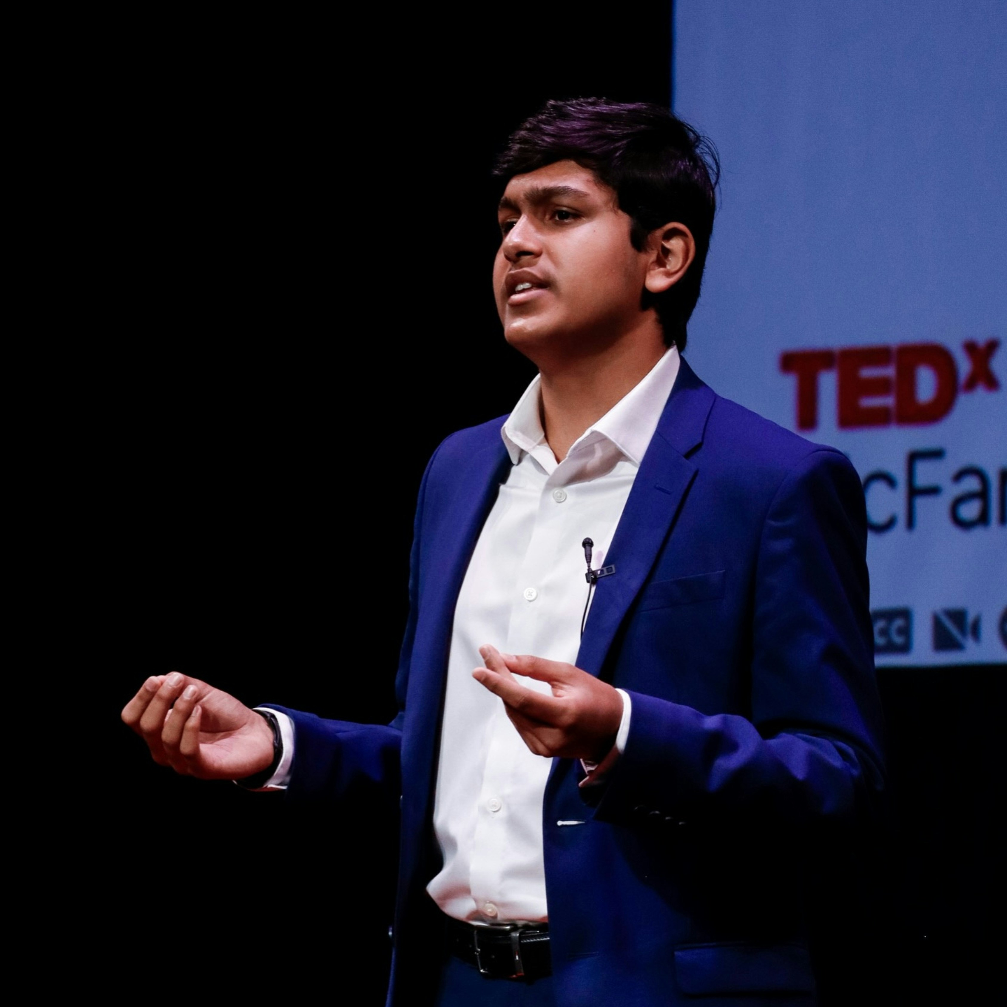 Pria muda berjas biru berbicara di panggung tedx.