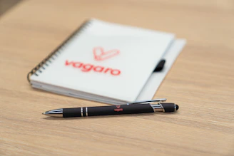 Pen and notebook with vagaro logo on a wooden surface.