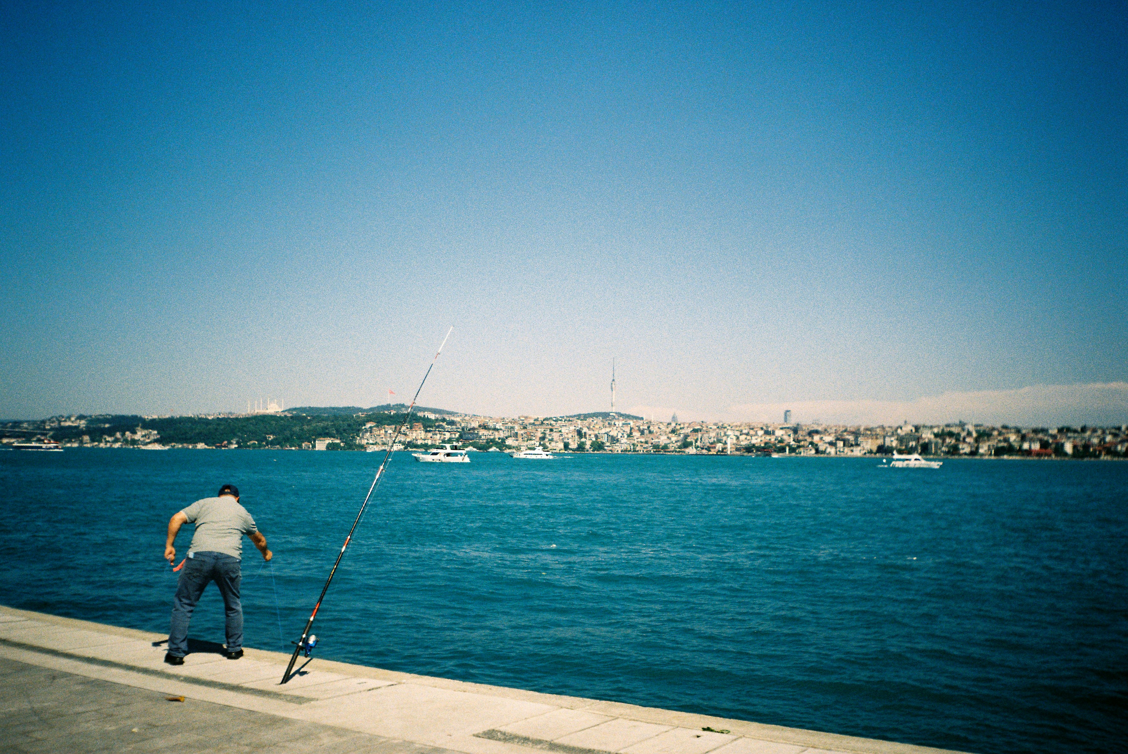 Man fishing by the water with a distant city skyline